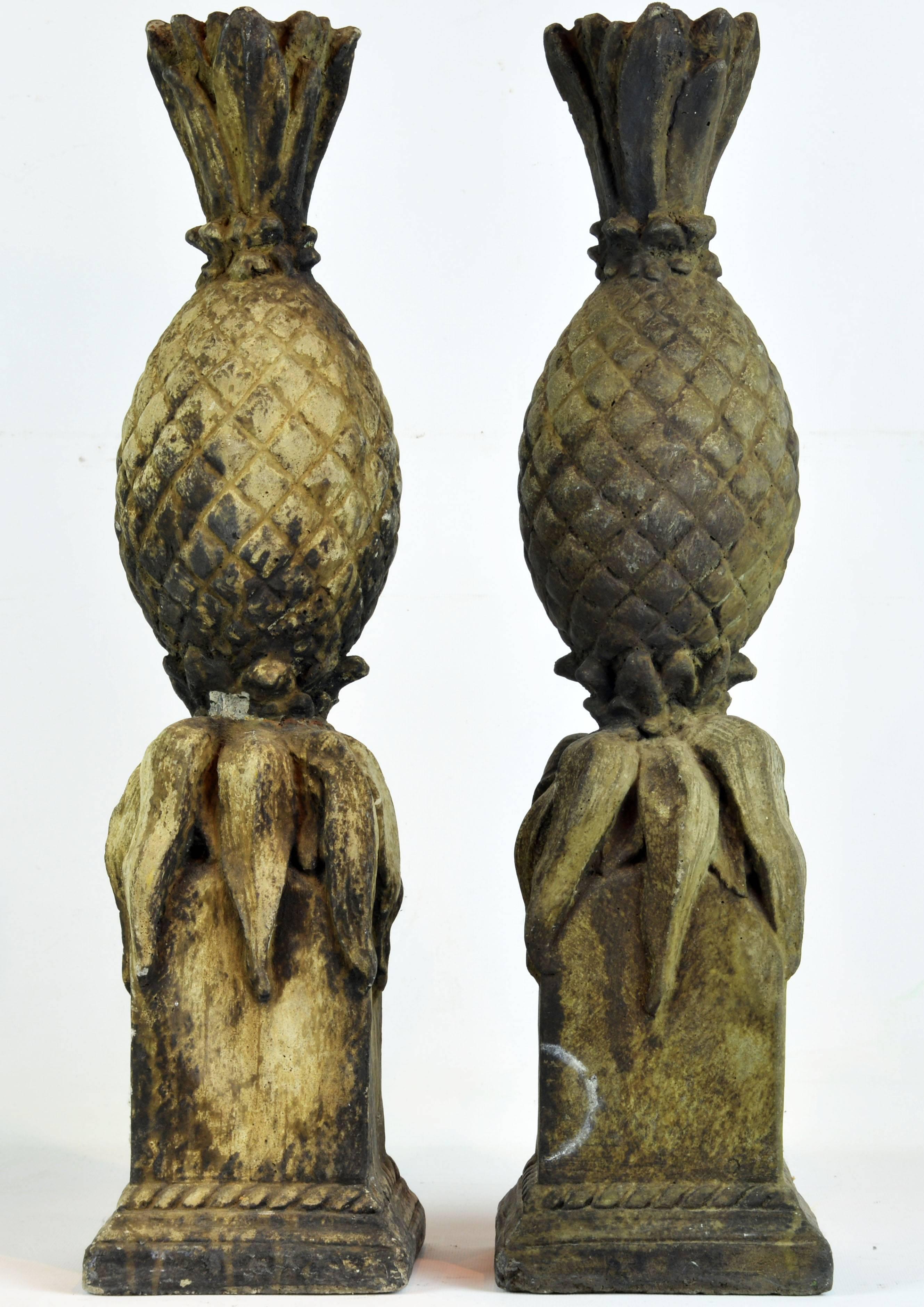 Standing 22 inches tall this attractive pair of antique cast stone statues of pineapples are raised on classical square stepped bases with rope friezes.