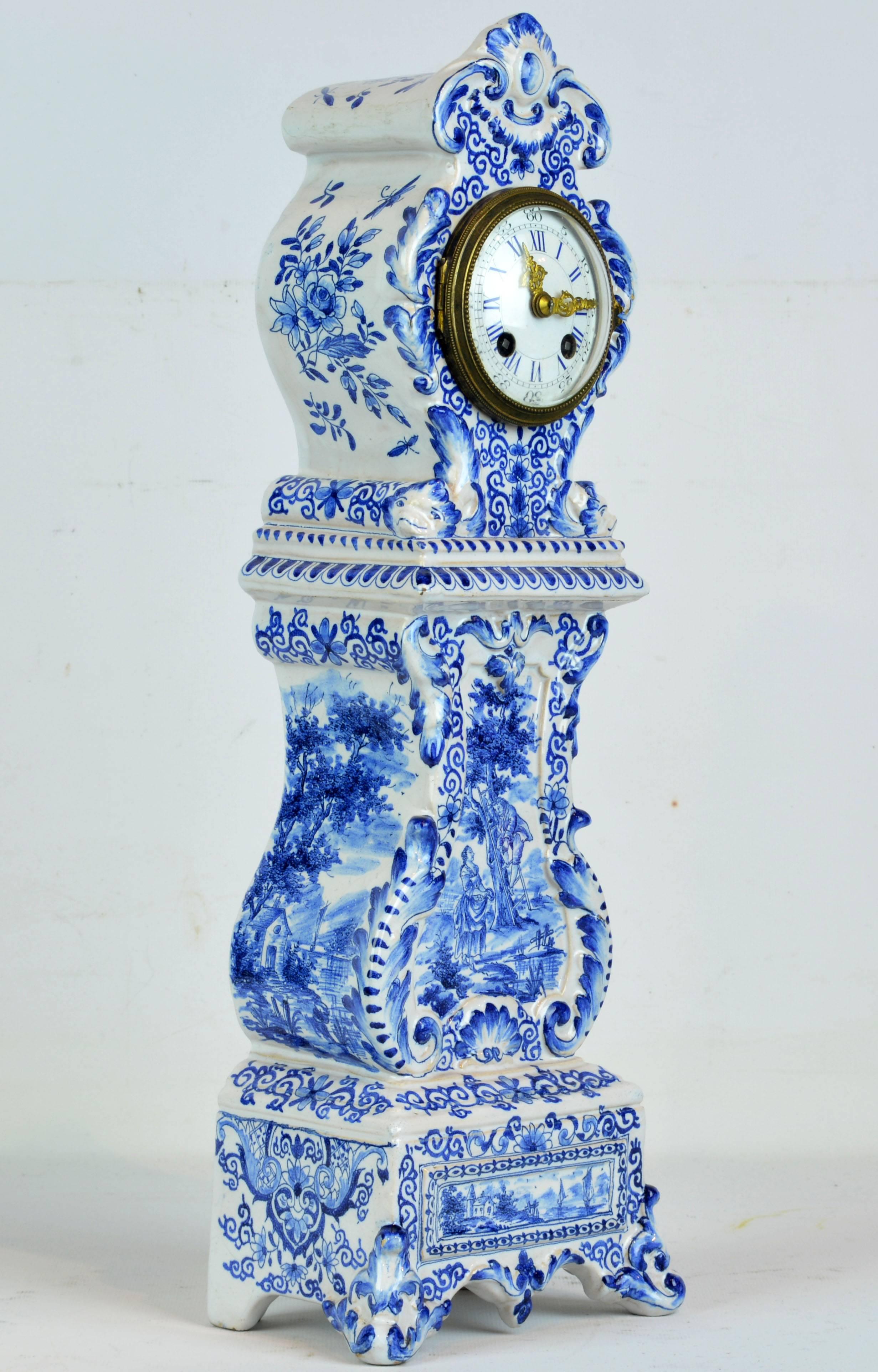 Standing about 18 inches tall this diminutive tall clock in the Rococo style features blue under-glaze decorations representing landscape motifs, scrolled leaf-work and floral designs. The clock is marked 'Burks Fabrikat' and is in working order.