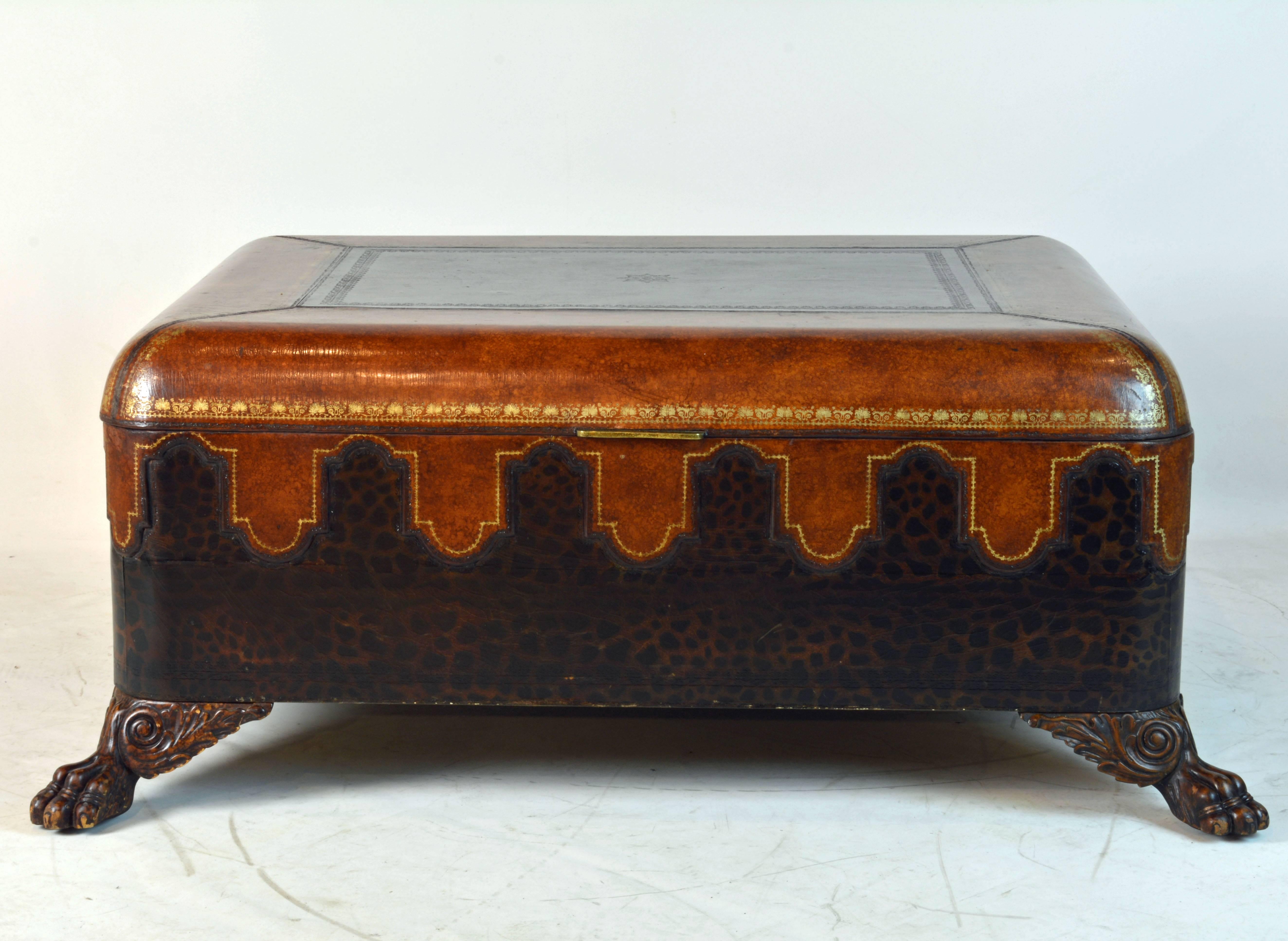 The body covered with oriental styled tanned and gilt tooled leather, top and bottom with darker leopard imprinted leather. Beautiful patina. Resting on four elaborately carved lions paw feet. The top open up to a full size lined compartment with