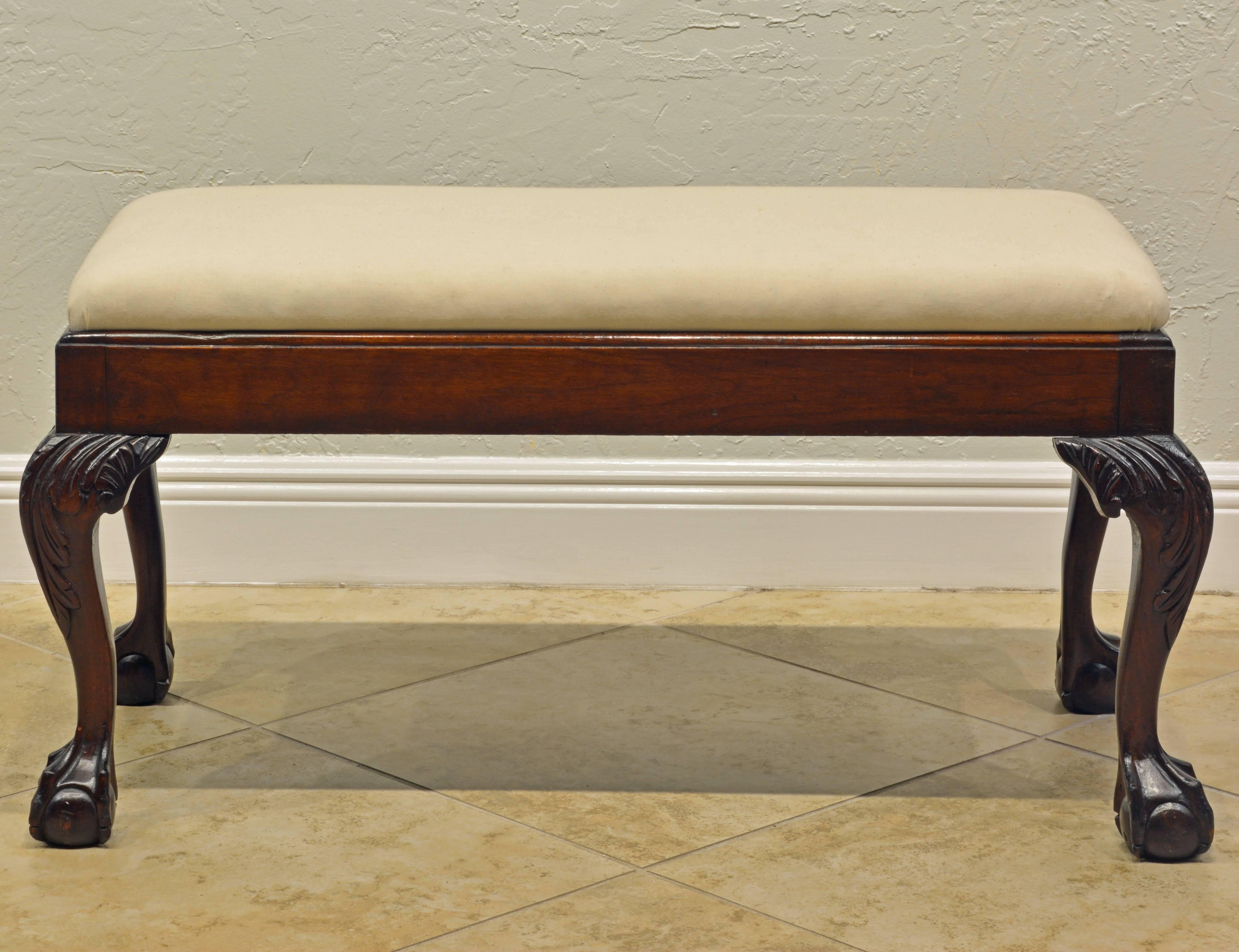 This great bench features a detachable upholstered and muslin covered seat resting in a frame supported by four carved cabriole legs ending in sculpturally carved claw and ball feet.
