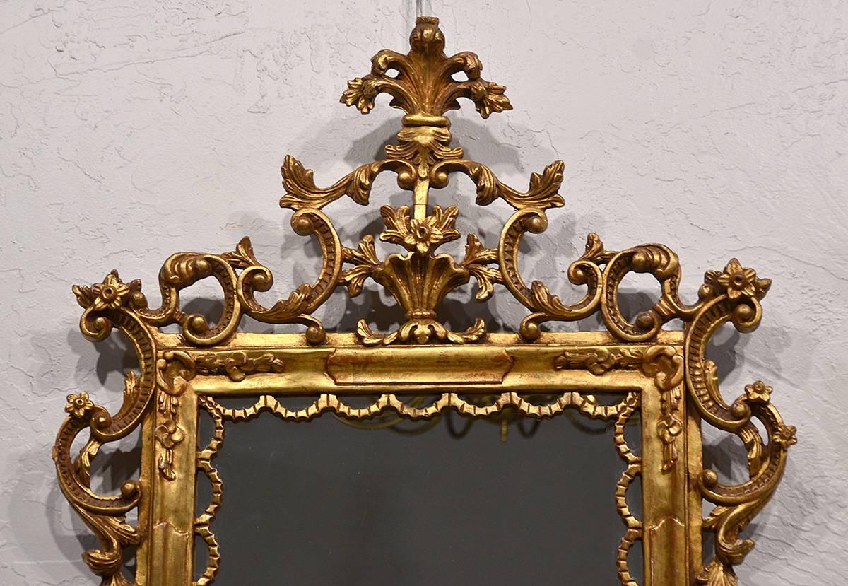 These Italian mirrors from the 1950's are elaborately carved in the baroque tradition with open leaf work and scrolls surmounted by a classical crest with vase and fleur de lis motif.