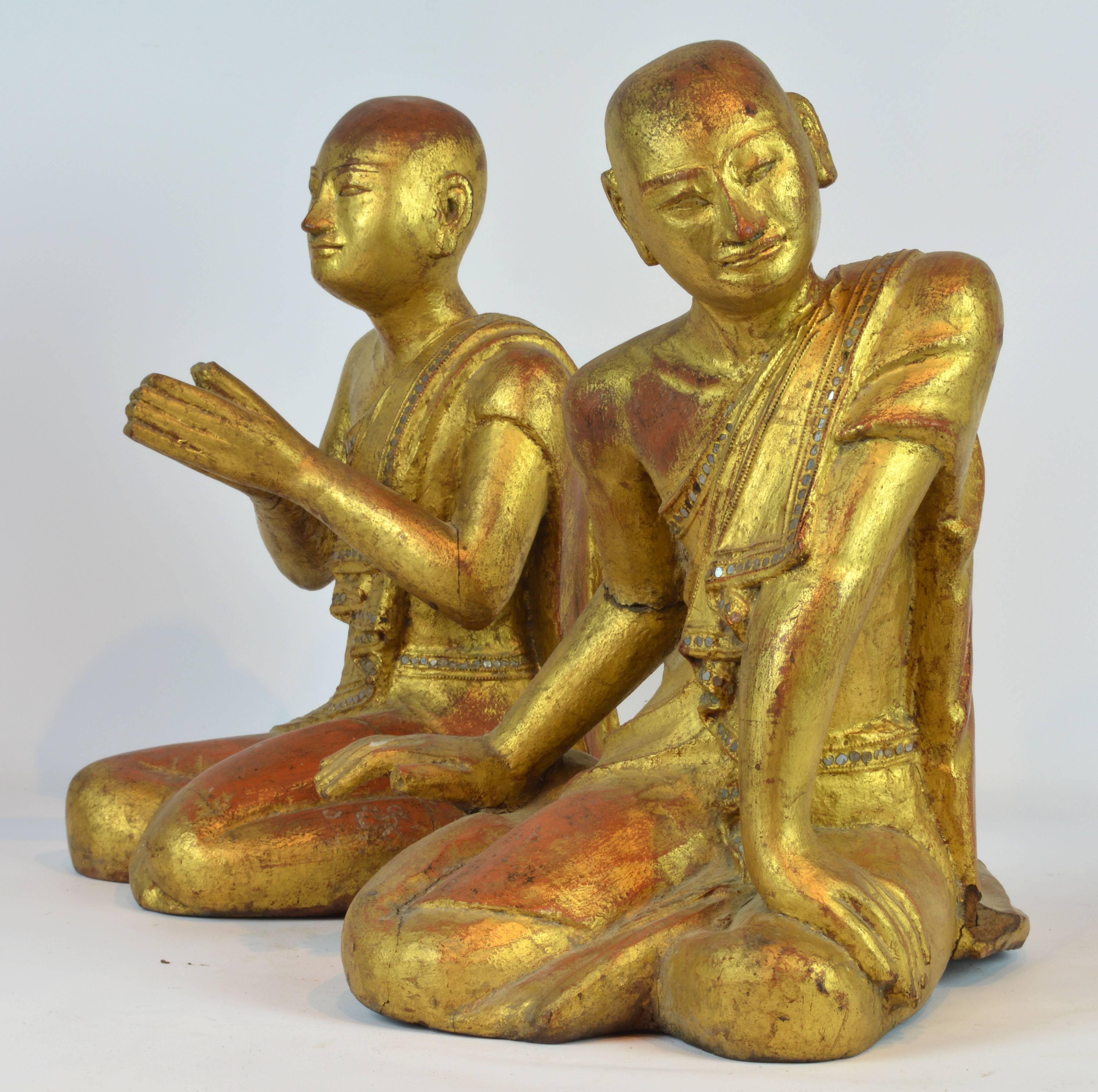 14 inches tall these two Thai or Burmese young monks are carved in wood and gilded. One monk is sitting in a praying position, the other with a relaxed but still devoted posture. The wear beautifully jeweled robes with inlay and intricate carved