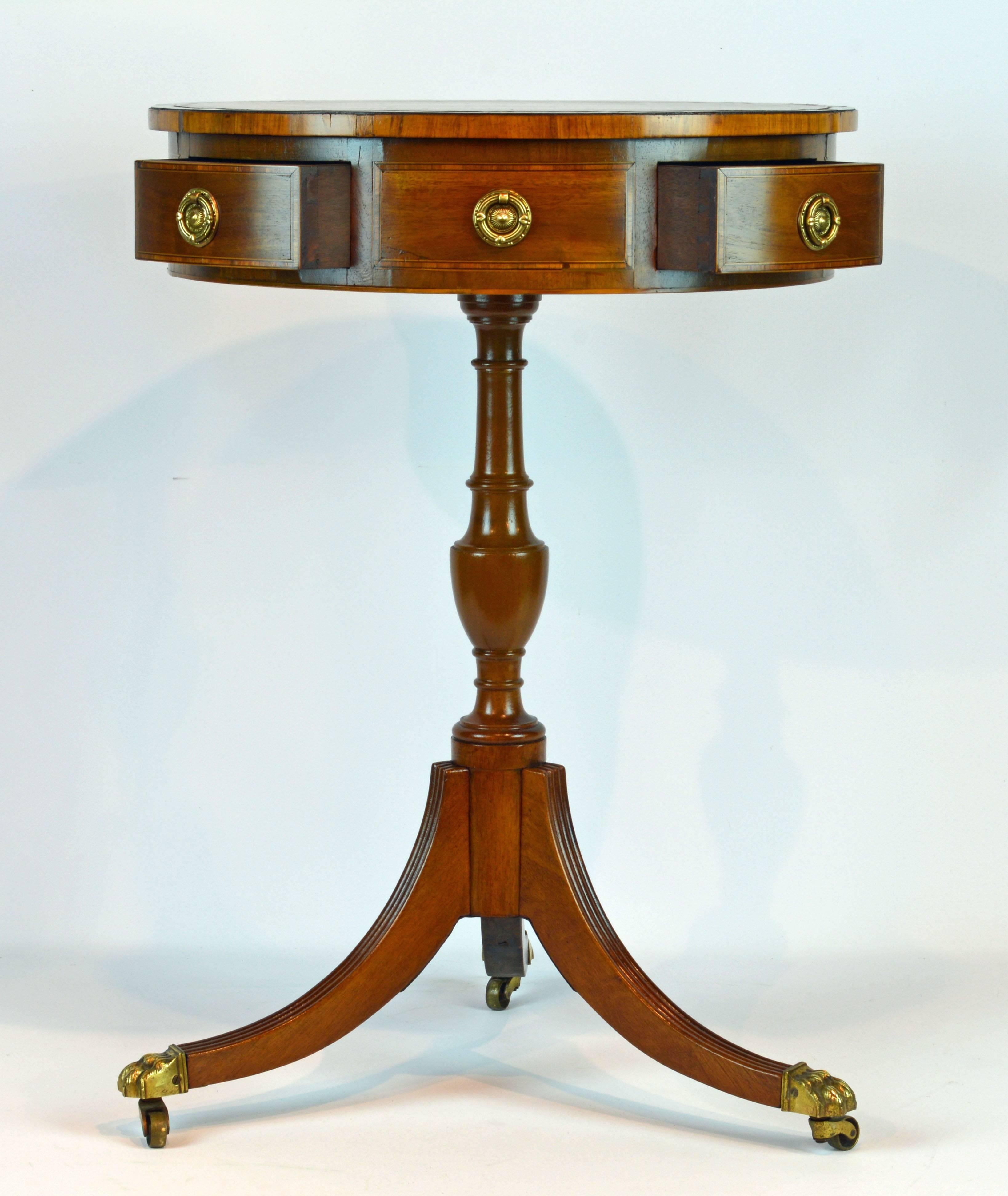 With a beautiful tanned leather top and four drawers alternating with simulated drawers this elegant crossbanded mahogany table rests on a turned and urn themed pedestal and three reeded splayed legs ending in lion's paw brass casters.