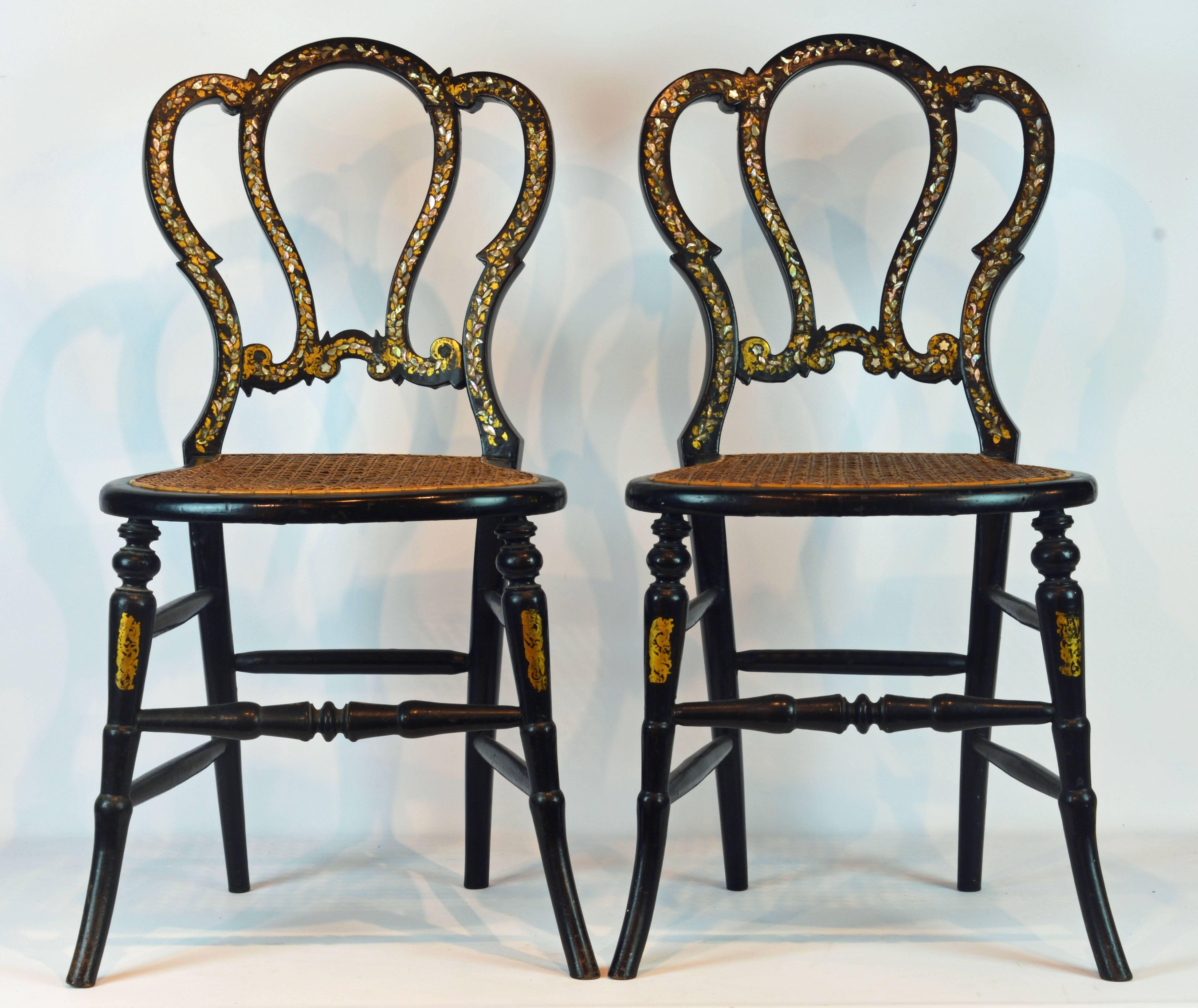 These chairs feature an elegant and romantic design made of carved wood, adorned by gilt vignettes and inlaid with mother-of-pearl. The caned seats are in good condition. The date to the 1880s England.