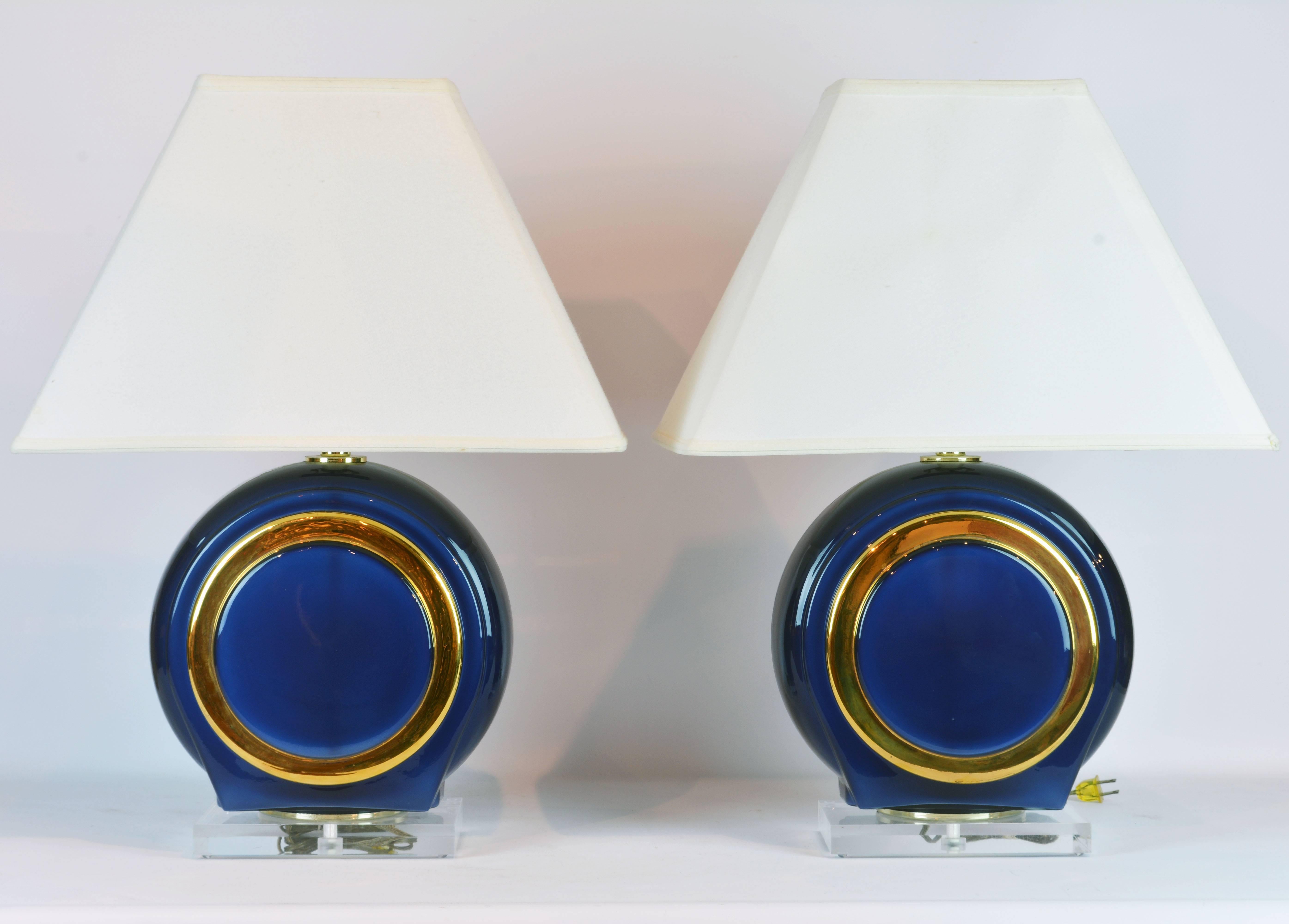 A tasteful pair of blue glass table lamps with circular gilt decor on square thick Lucite bases. The lamps look great even during day when the daylight shines through the blue glass. The measurements below are including shade.