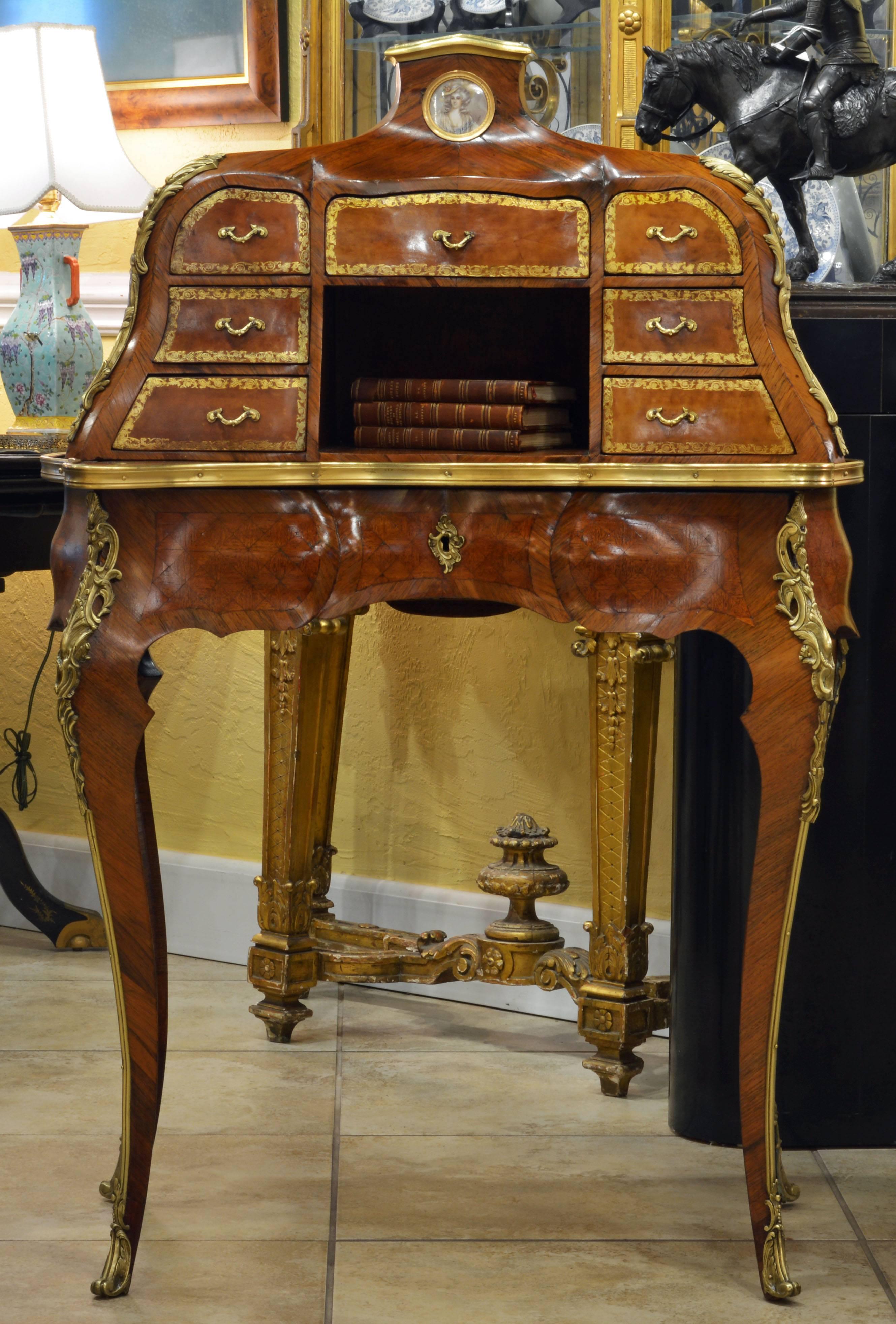 This excellent French Louis XV style bureau à gradin or ladies writing desk features an upper curved and shaped structure surmounted by a miniature portrait on ivory above seven gilt=leather fronted small drawers centering an open compartment. The