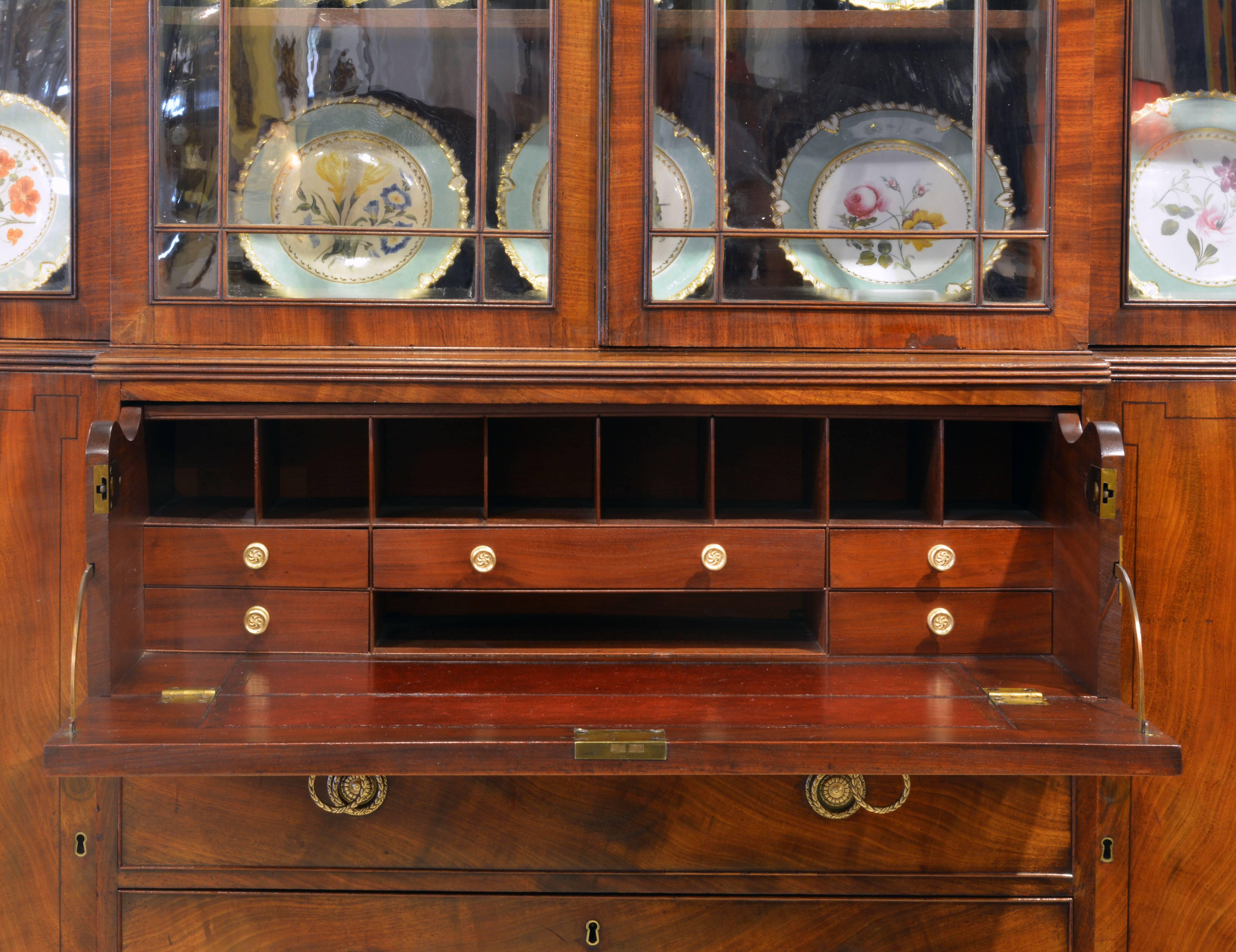 This stately secretary bookcase of great proportions features a central drawer which upon pull out opens up to an interior fitted with smaller drawers and open compartments above a burgundy red and gilt tooled leather writing surface. The four