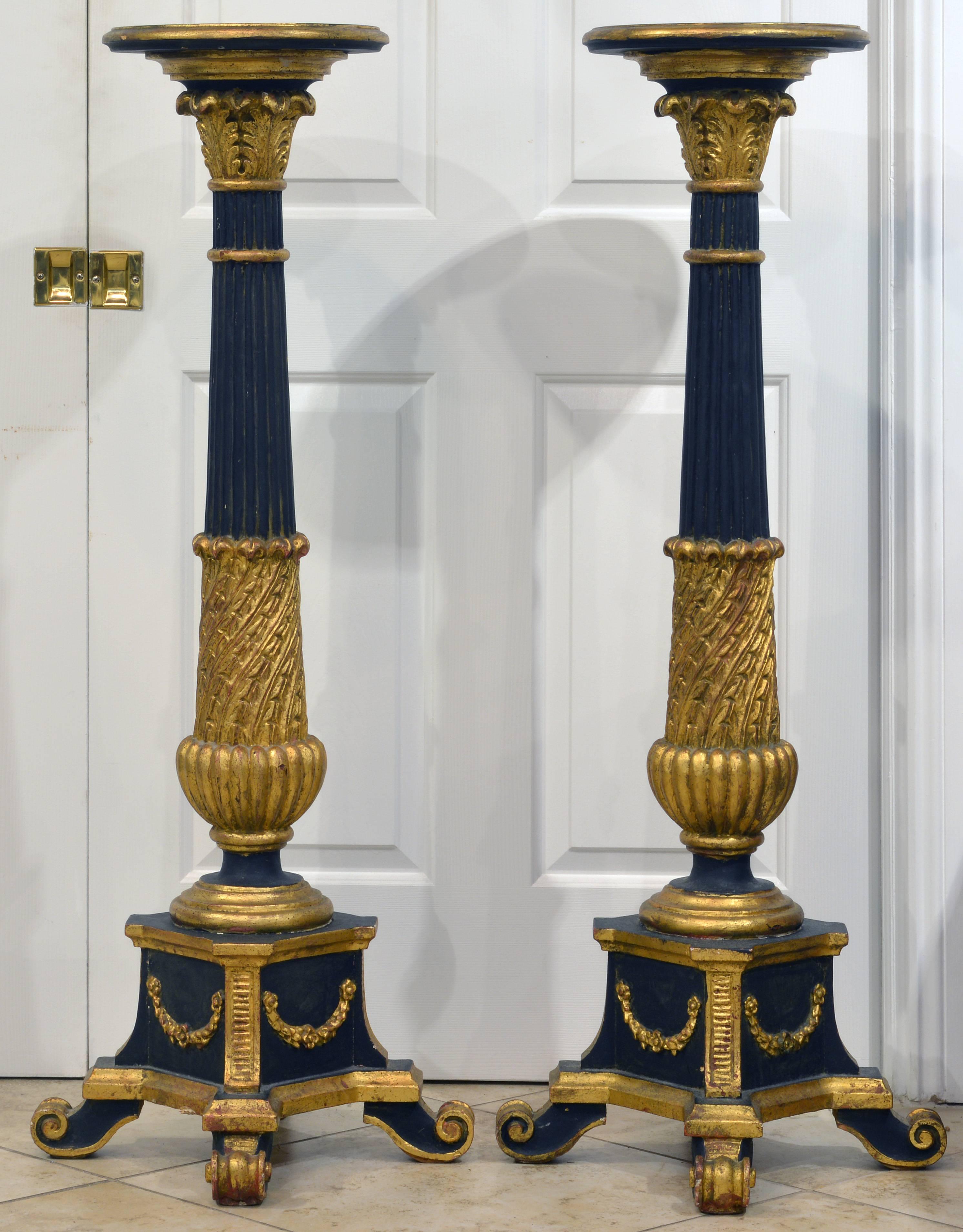 This pair of palatial looking pedestals feature circular tops above reeded and ebonized columns adorned with carved giltwood capitals and baluster shape lower sections set on square bases with giltwood garlands and resting on carved volute feet.