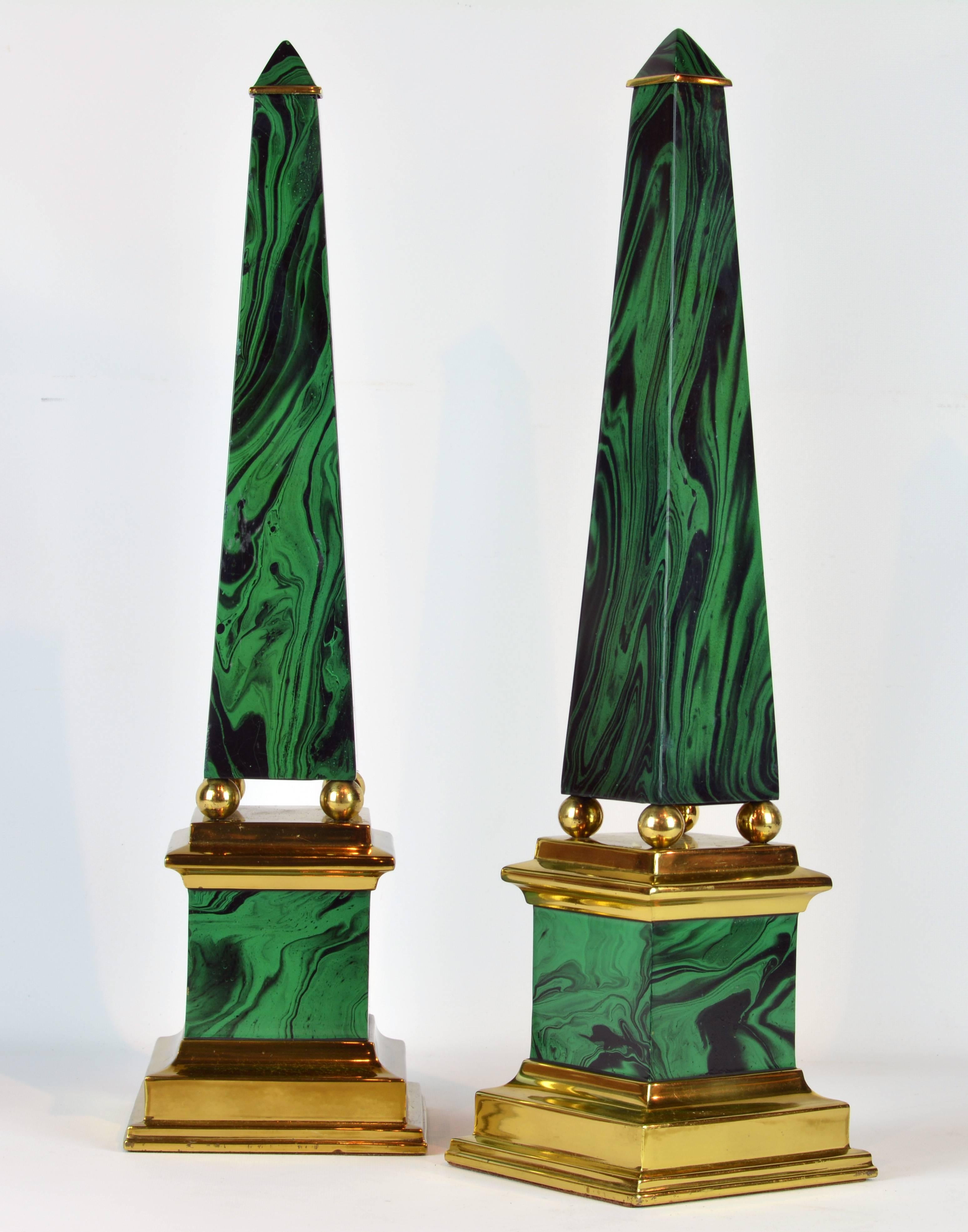 Standing almost 22 inches tall this beautifully crafted pair of obelisk models in the neoclassical style feature faux malachite enameled surfaces intersected by polished brass elements on the top, between shaft and bases and as stepped foot bases.