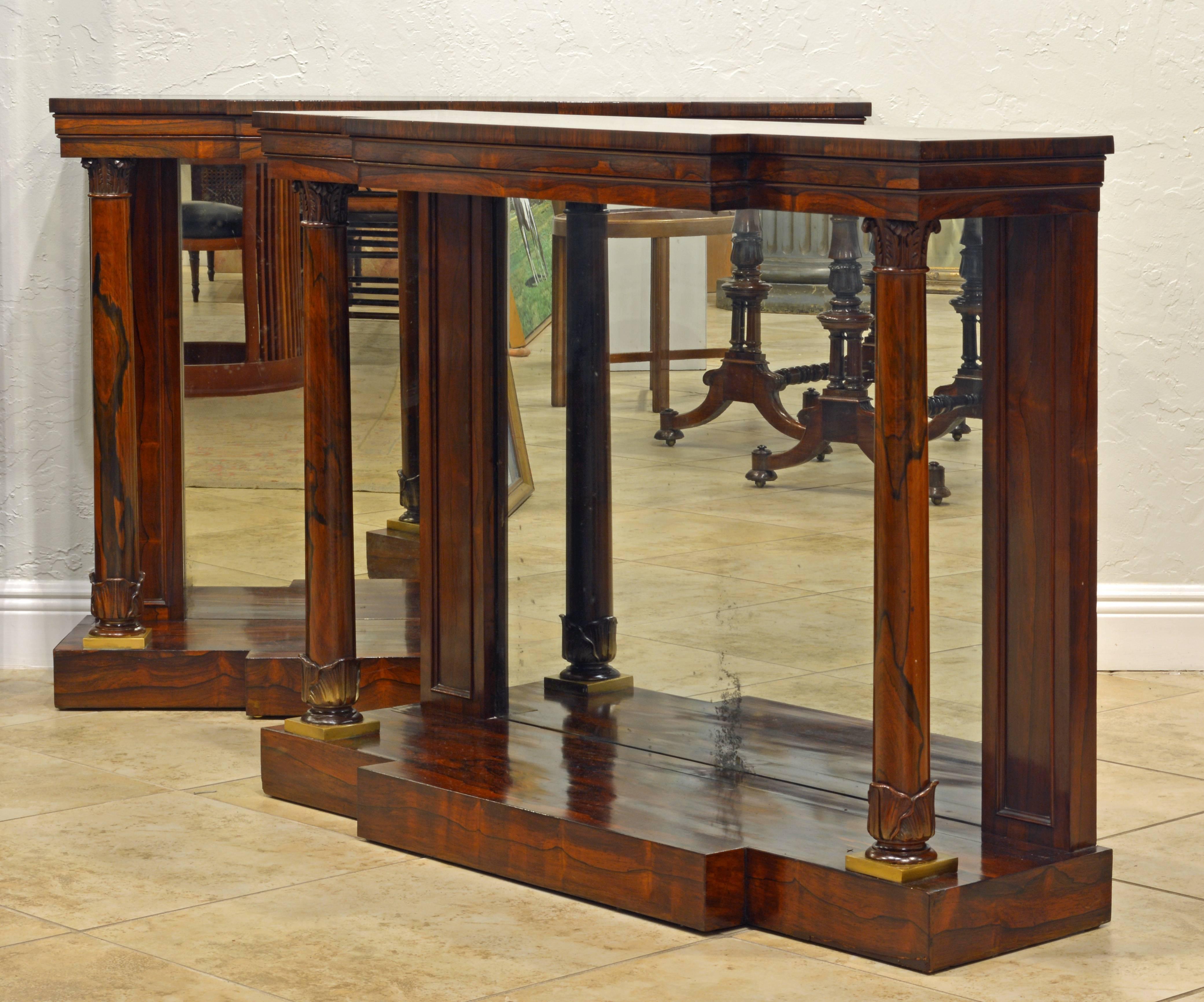 This rare pair of early 19th century Regency breakfront console tables feature string inlaid polished tops above profiled friezes resting on double columns with carved capitals and bases flanking mirrored back panels and standing on a plinth bases.