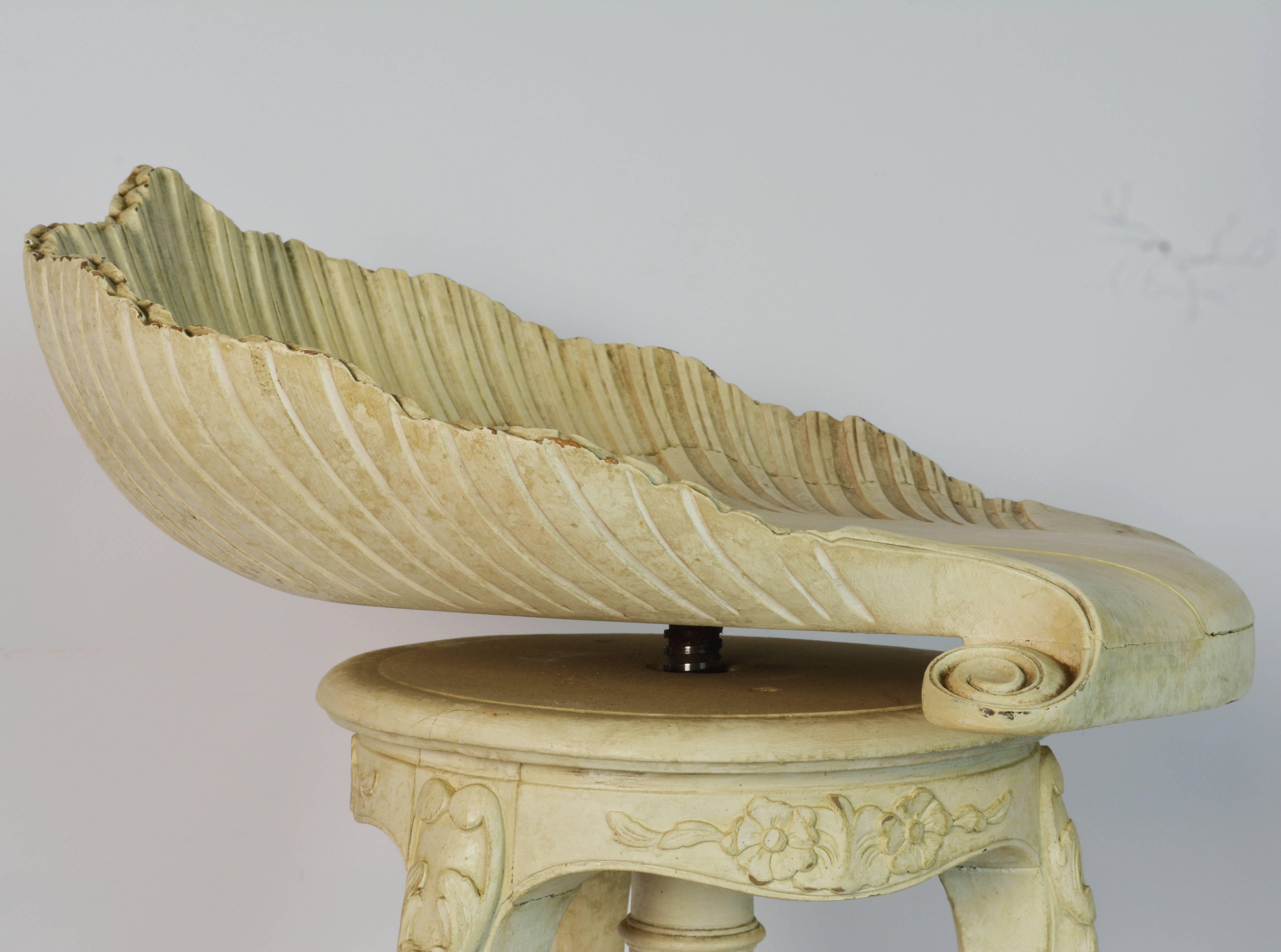 This carved and painted stool feature a sea shell shaped seat which by a swivel is adjustable in height appropriate for a piano stool. The seat is raised on a central support and three carved legs ending in paw feet and resting on a slightly