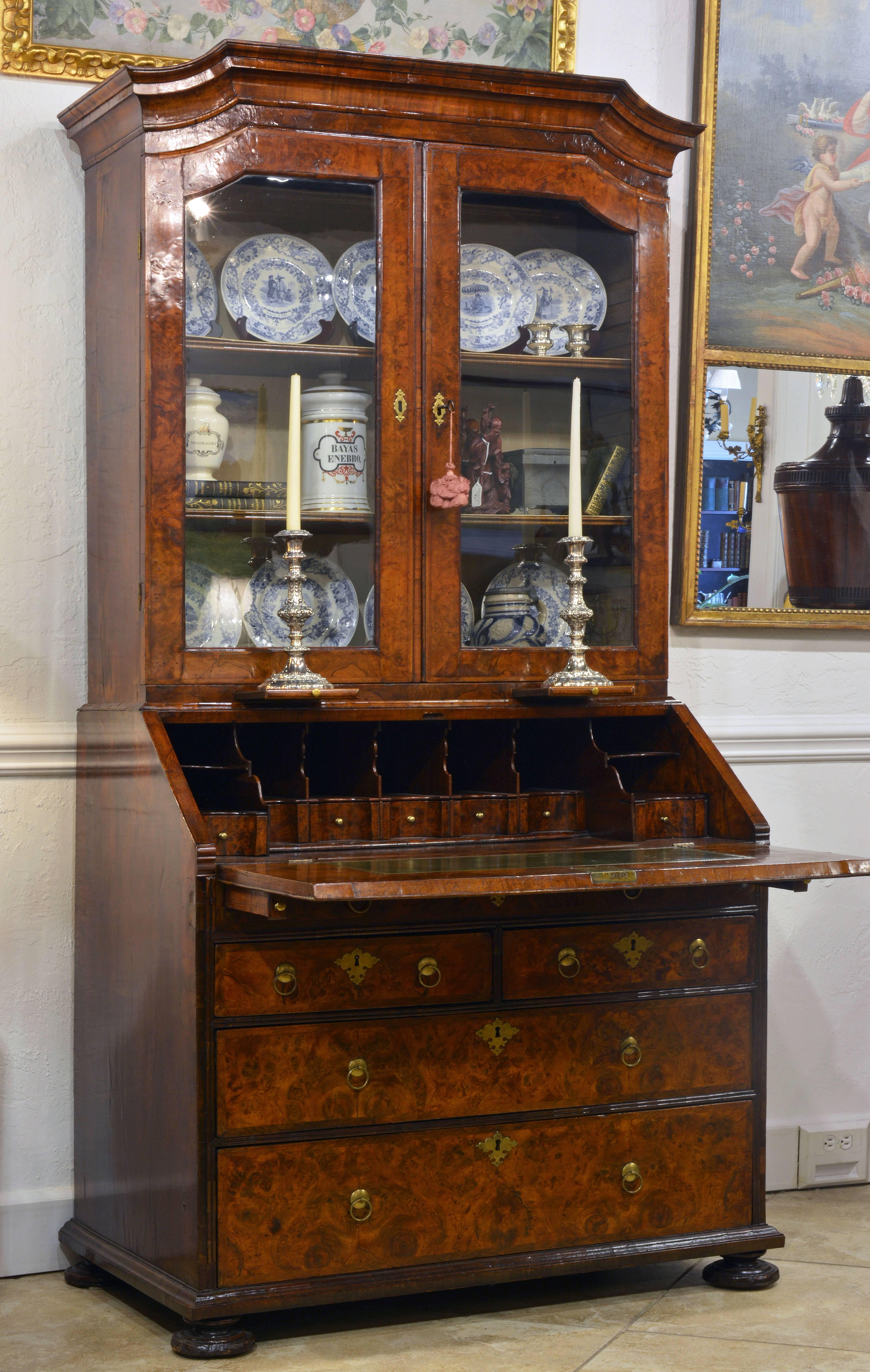 This charming two part secretary bookcase features a Dutch inspired corniche above glazed doors enclosing a silk lined interior with adjustable shelving. Right under the doors two pull-out shelves offer the possibility of placing candlesticks. The