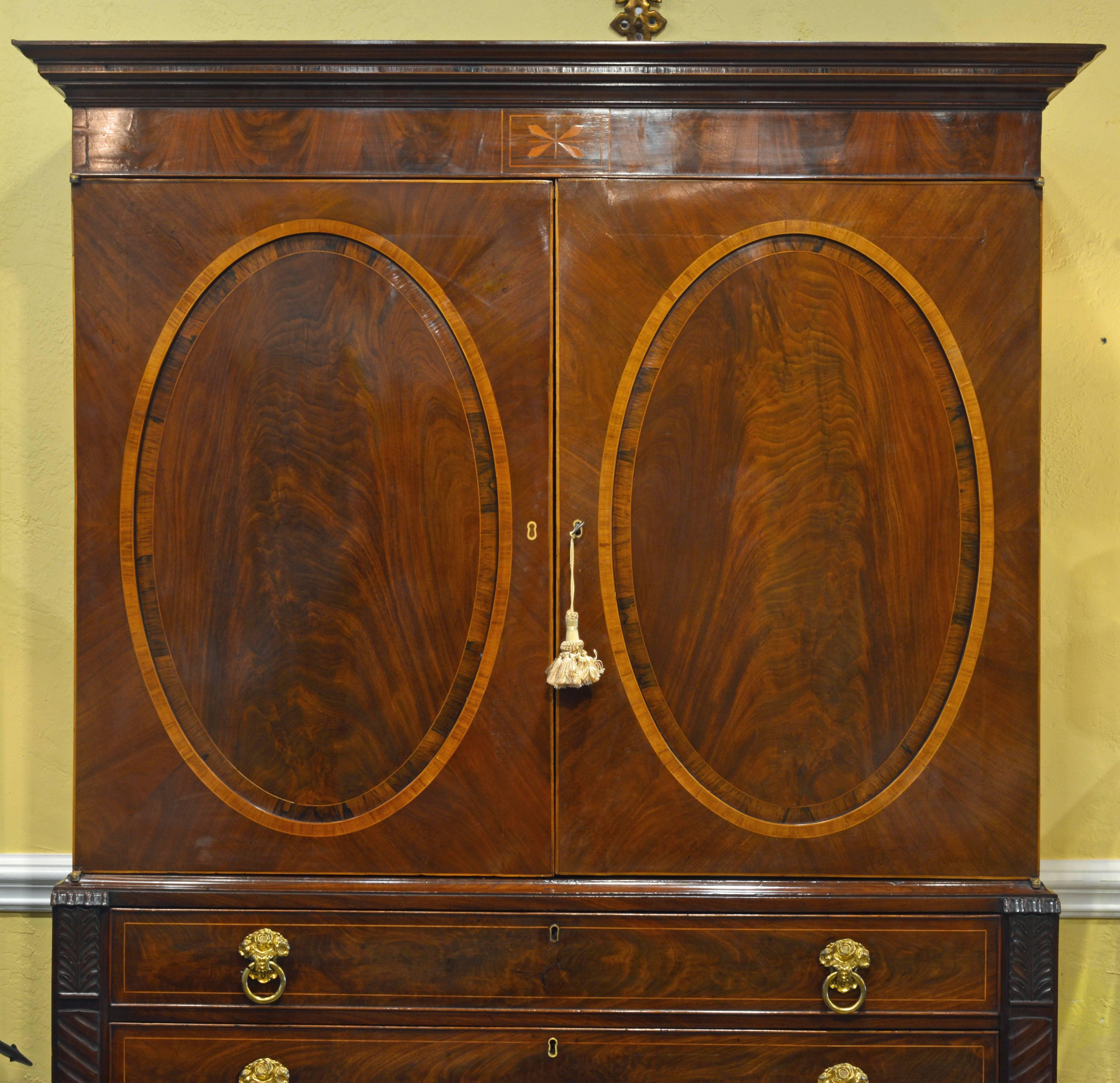 This excellent linen press dating from, circa 1830 features a Classic cornice above two oval paneled doors inlaid with boxwood and satinwood opening up to an interior that has been shelved but is now open for other purpose. The lower part features