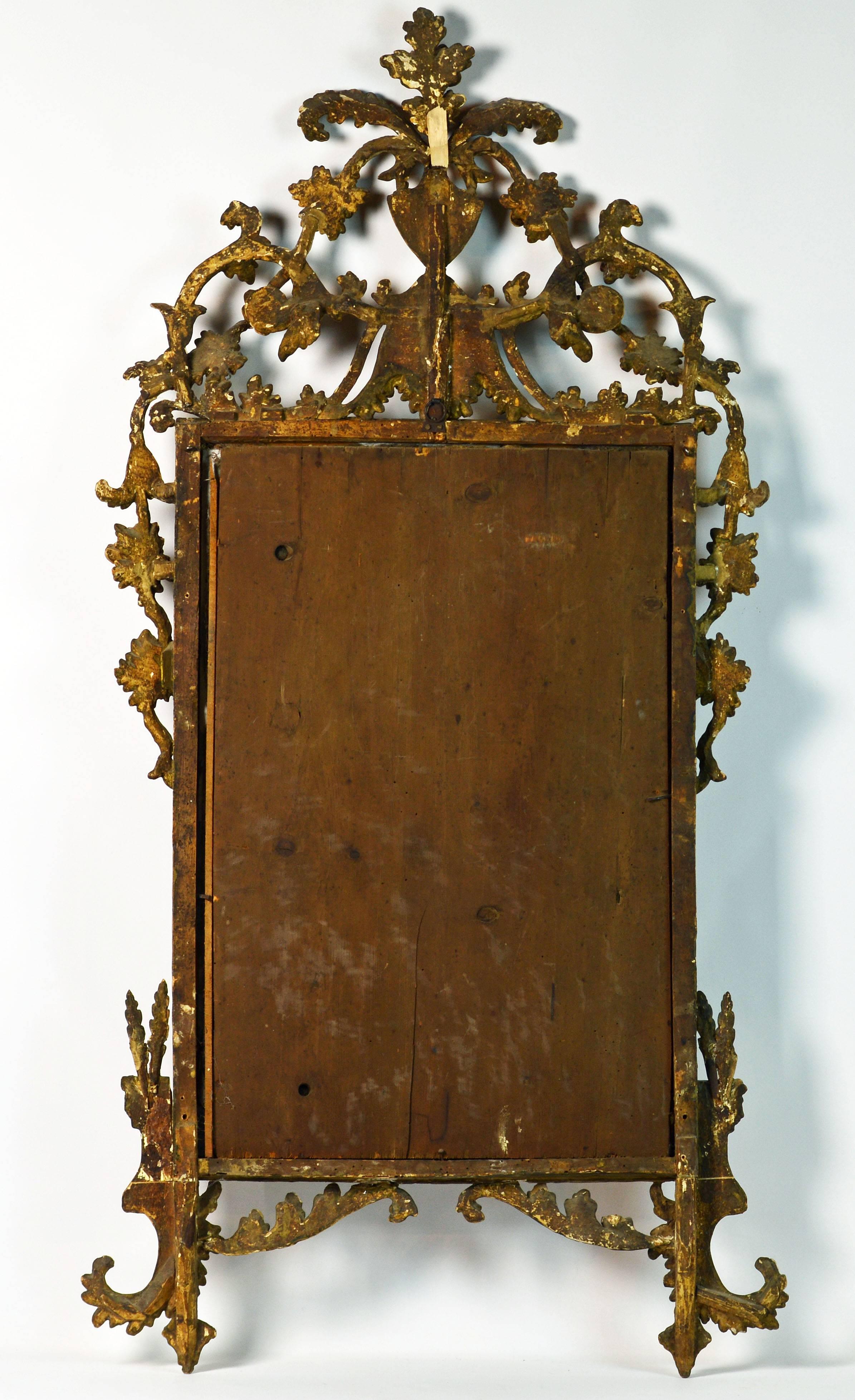 59 inches tall this extraordinary mirror features expansive openwork carvings of leaf work, figures, garlands, urns and scrolls in the rococo tradition. The glass is original and so is the painted surface with traces of gilt.