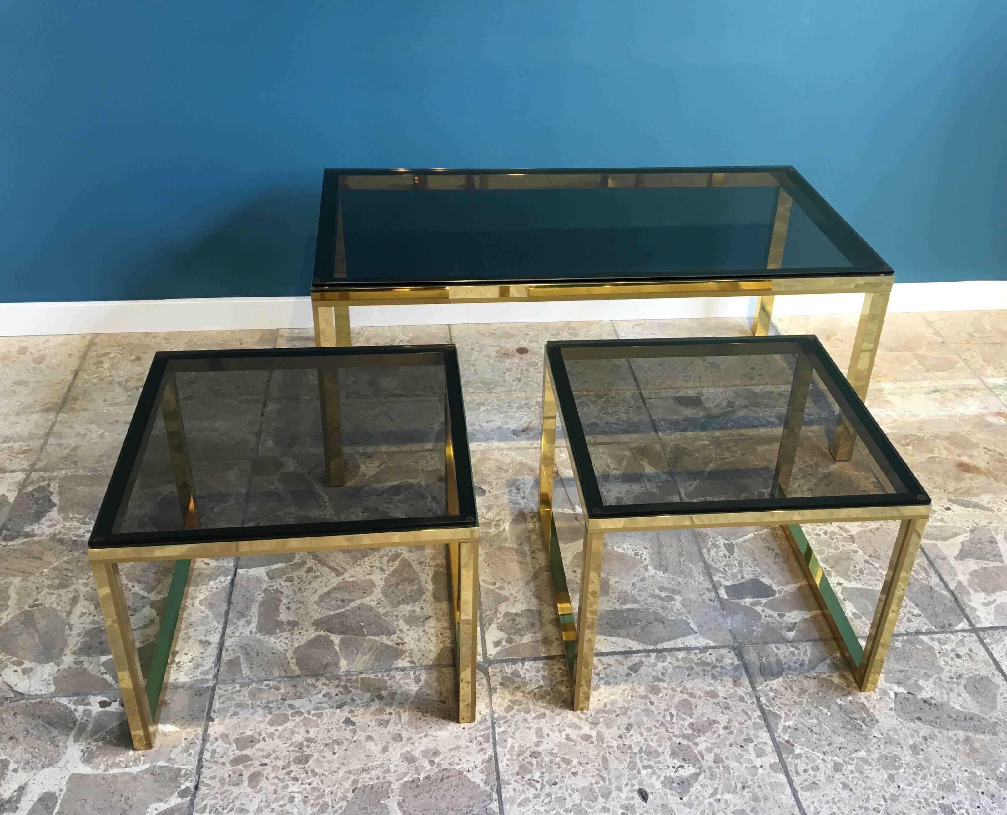 This set consists of three tables. Each features a frame made of brass and a top made of smoked glass. The tables appear to be made in the 1970s or 1980s in Europe. The large rectangular table measures 110 cm width and 45 cm. The two square tables