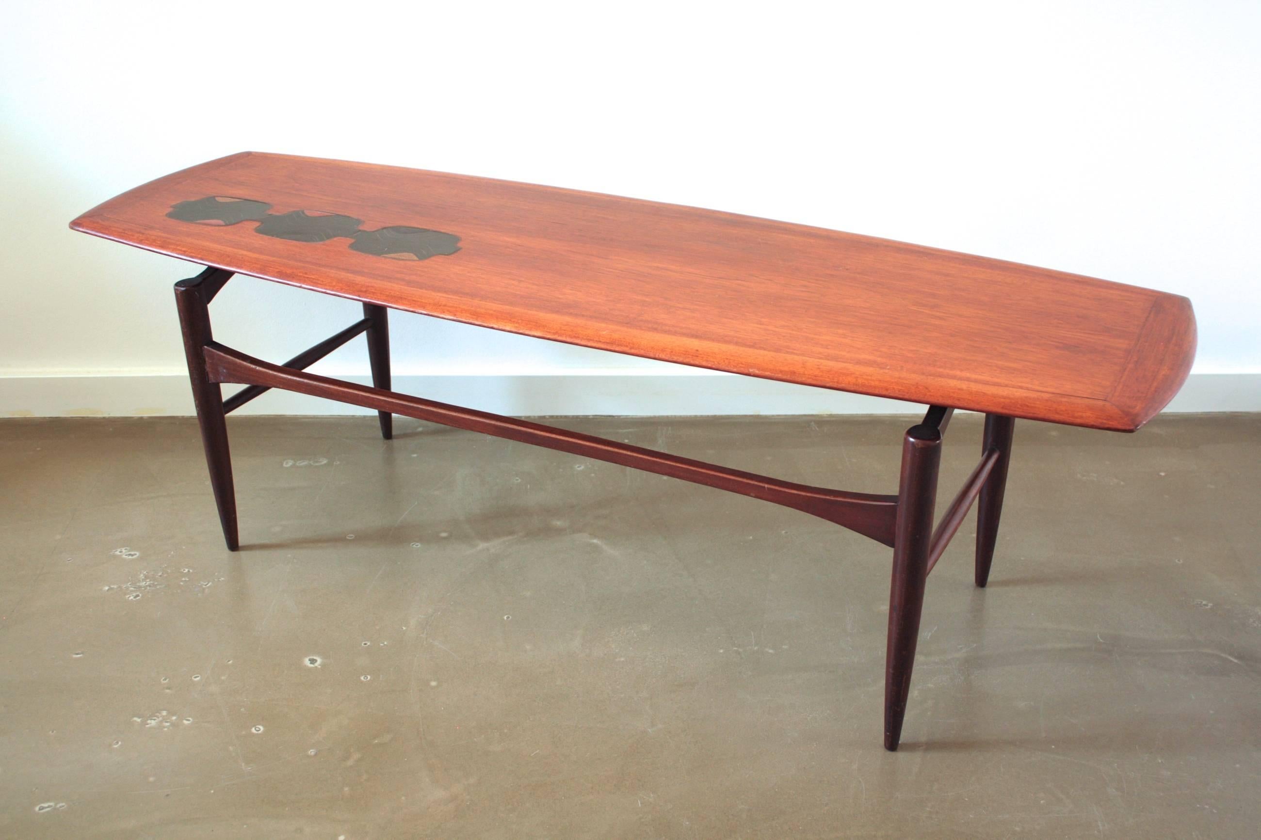 This coffee table is made from teakwood and was produced in the Netherlands in the 1960s. The top is rectangular and has rounded edges. It features three black inlay-like elements in the table top.