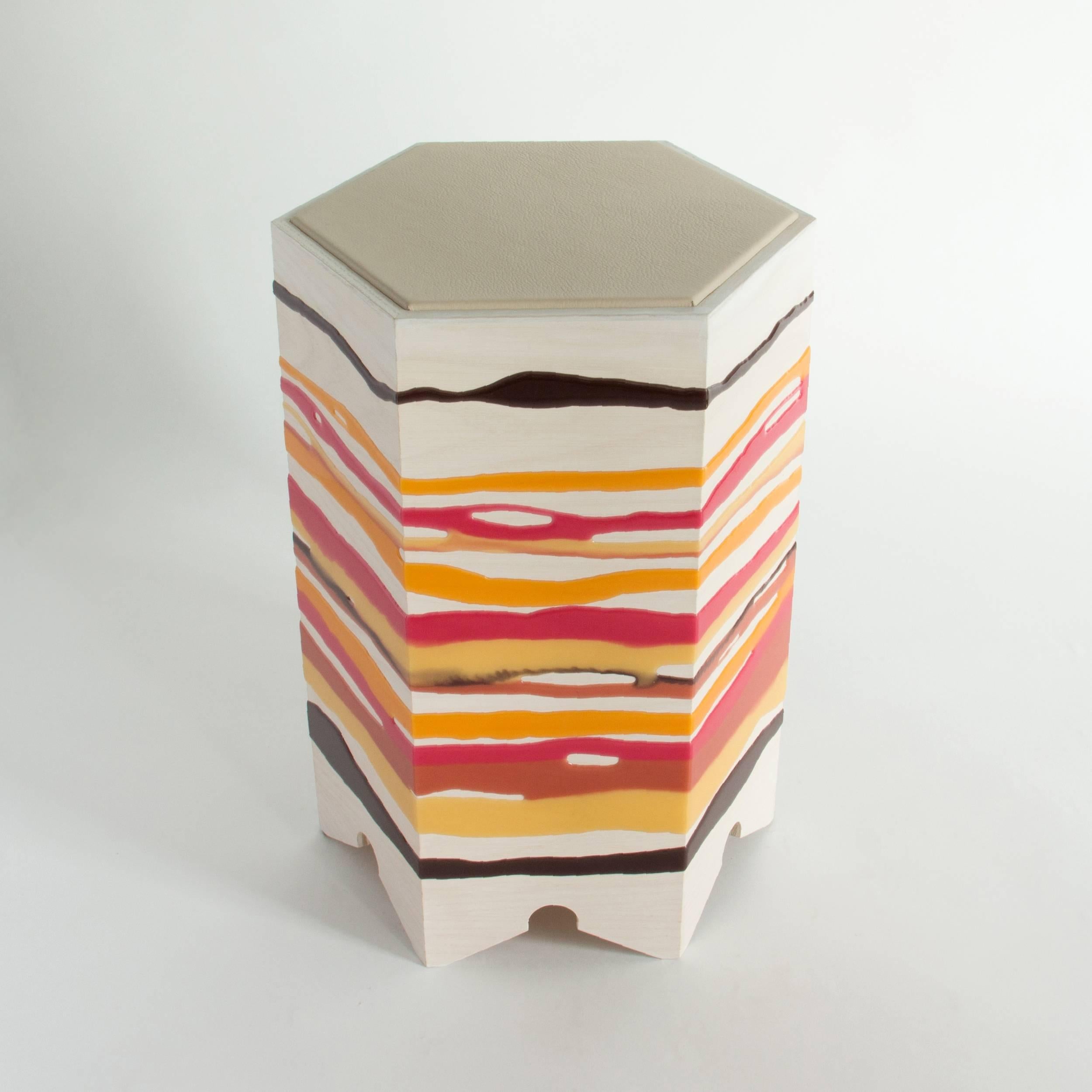 The drip or fold side table by Noble Goods is constructed of a single sheet of ash plywood that has been hand-dripped with liquid resin, then bent into a hexagonal shape. Finished with a leather upholstered top. The hot colors of this piece are
