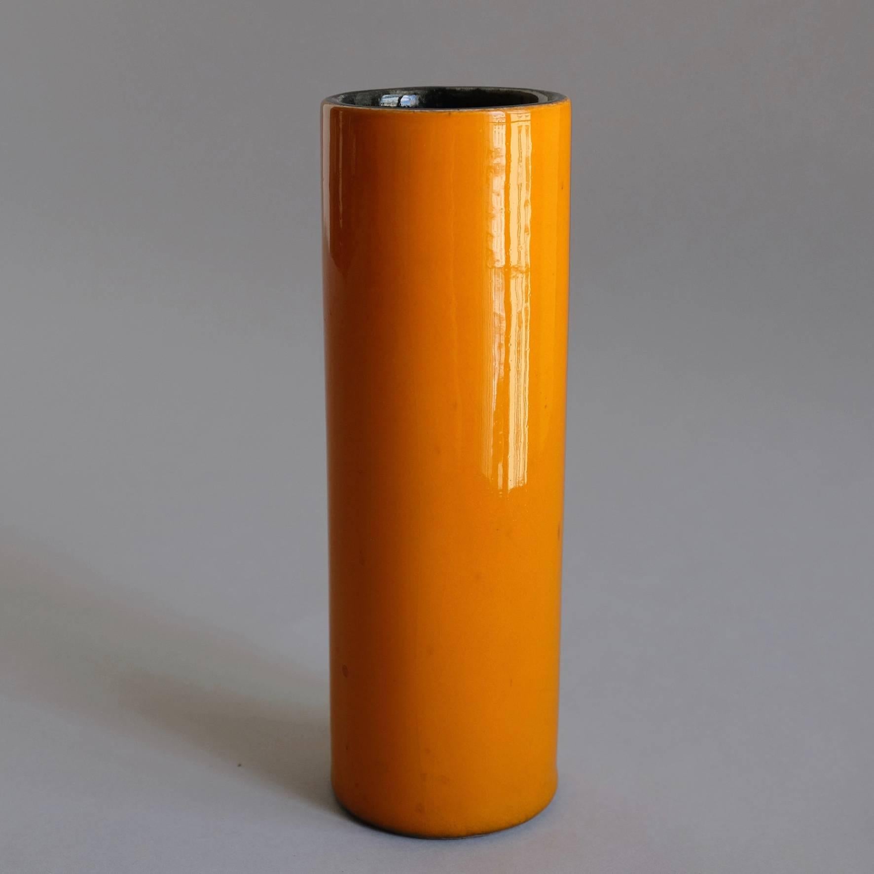 An orange glazed ceramic cylindrical vase, with a black covered interior.
Signed underneath 