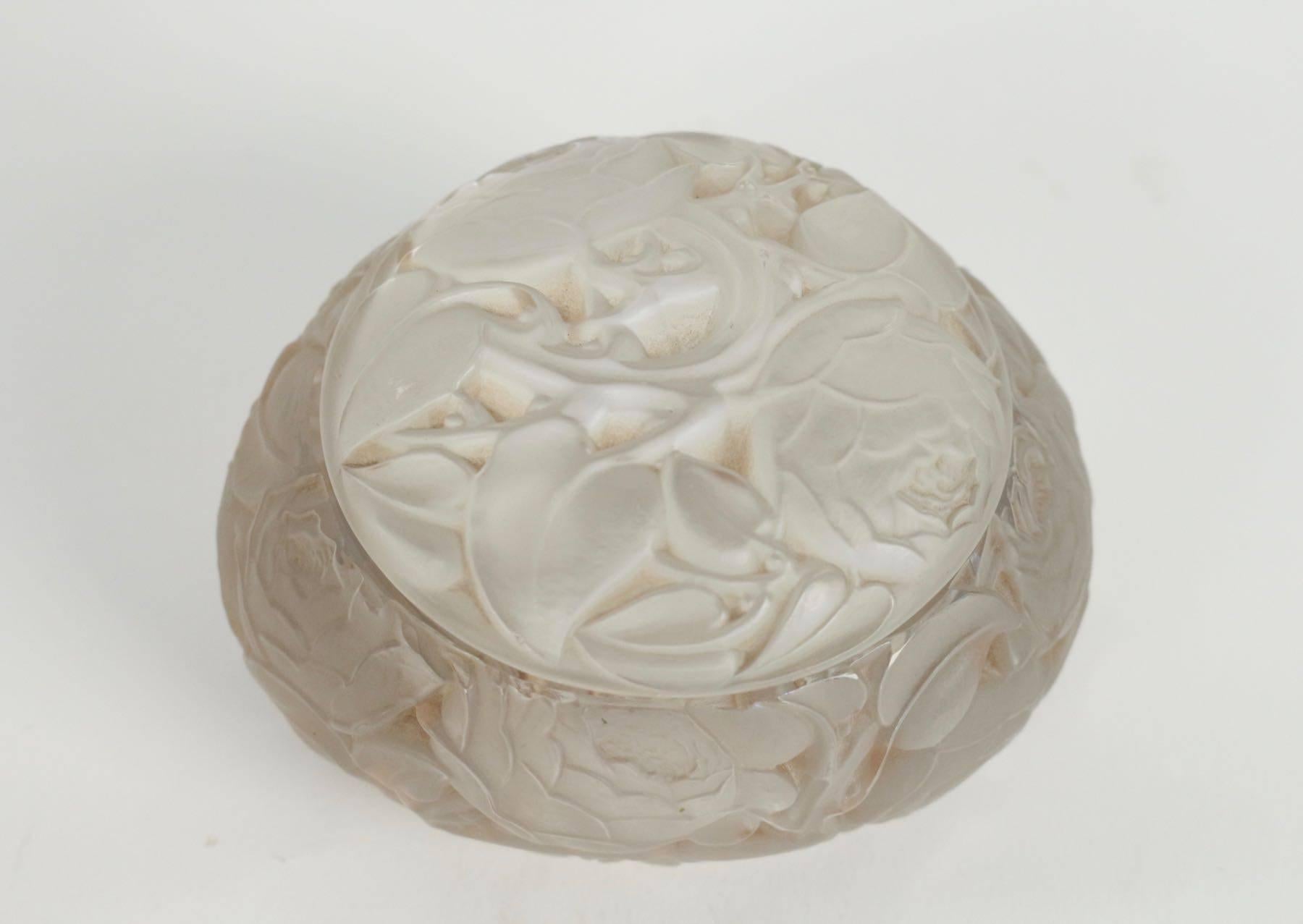 Thickly two parts fully rose covered frosted glass oval box with shallow lid.
Heavily molded rose flowers decorated glass.
Highlighted with sienna staining.
Measures: 13 cm long oval 8 cm height.
Engraved R. Lalique, France.
Designed, 1927.