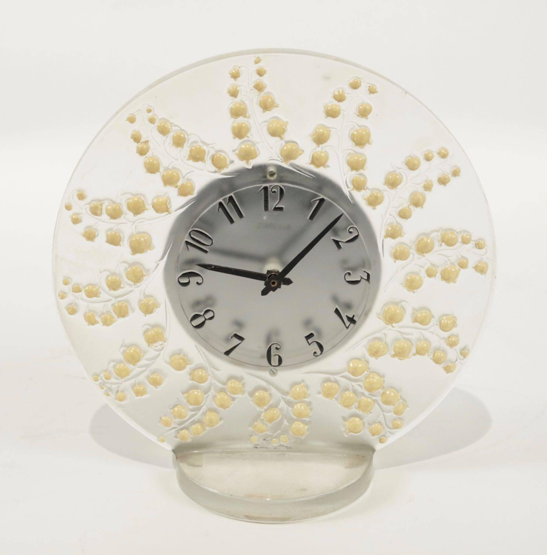 Rene Lalique clock Muguet: 
21 centimeters tall round clear mistletoe decorated glass around a central mechanism on an opposing round base
 design of lily of the valley white enemailed emanating from the center facewhite.
Mecanism Quartz working