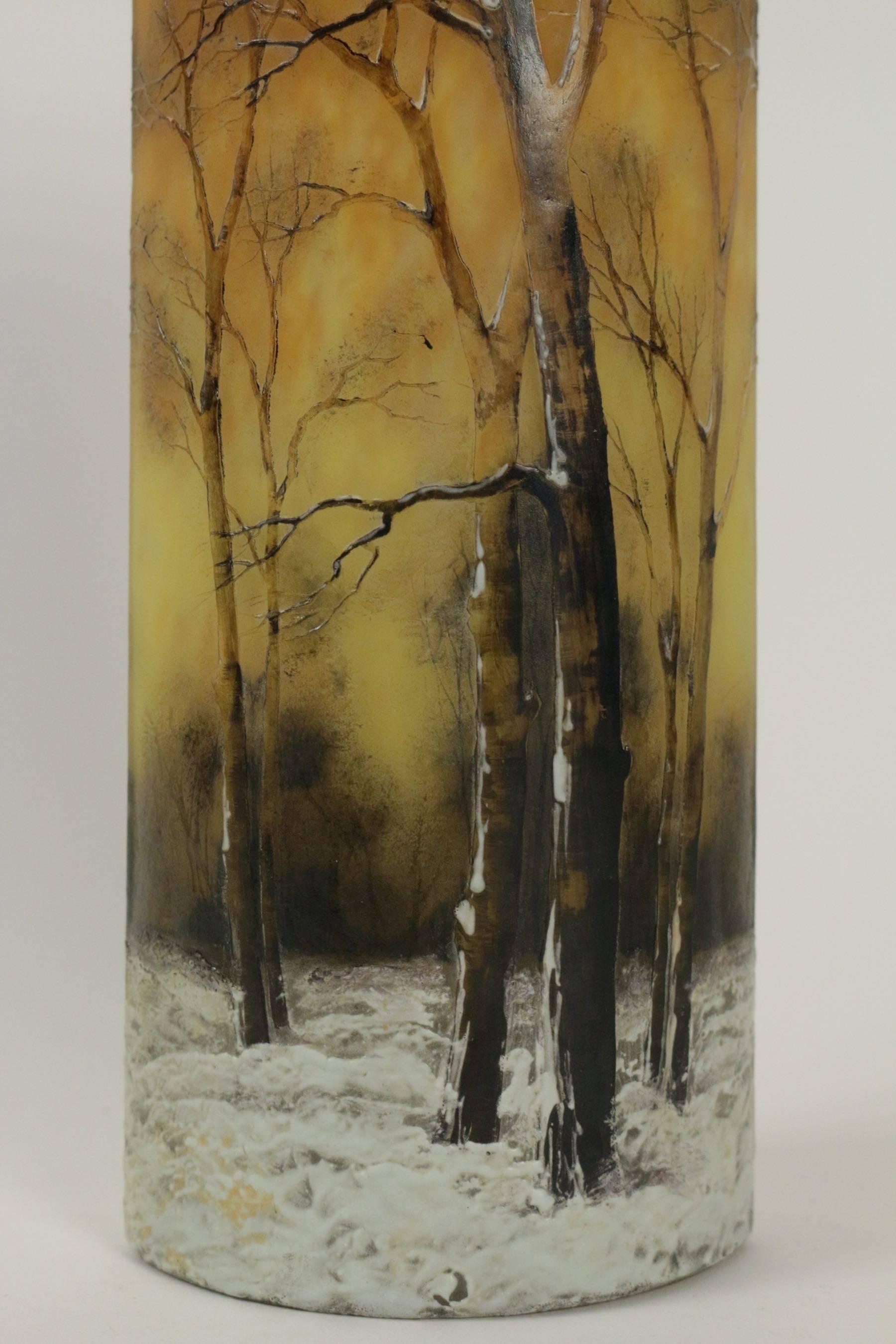 An enameled glass 'winter landscape' vase.
Enameled winter scene vase.
Daum vase has decoration of barren trees rising from snow covered ground against a mottled orange and yellow background. Trees are nicely enameled in shades of brown with white