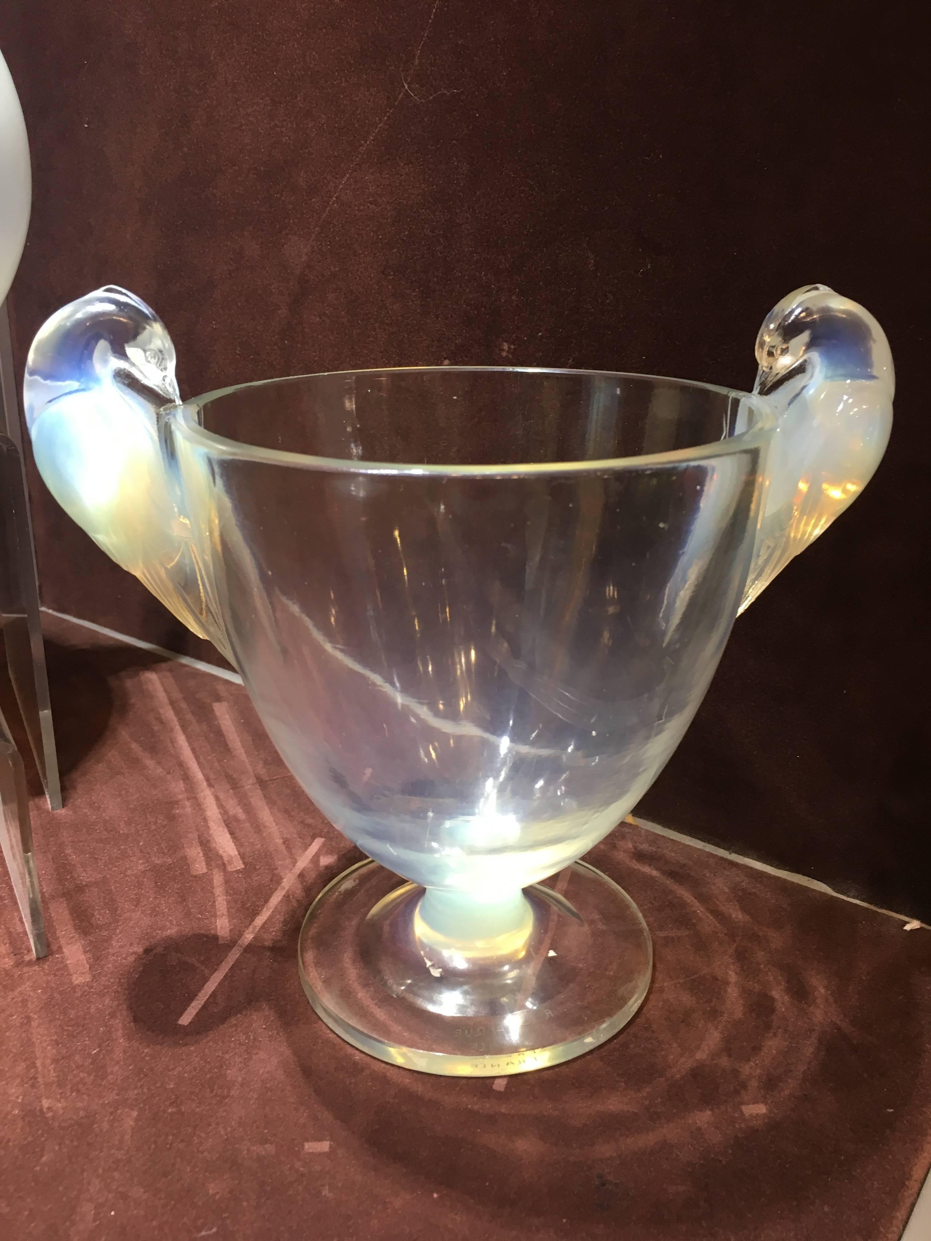 Opalescent footed goblet form glass with a bird rising above the rim on either side of the otherwise undecorated 
footed goblet form opalescent glass with a protruding bird perched on either side 
Signed and numbered 
