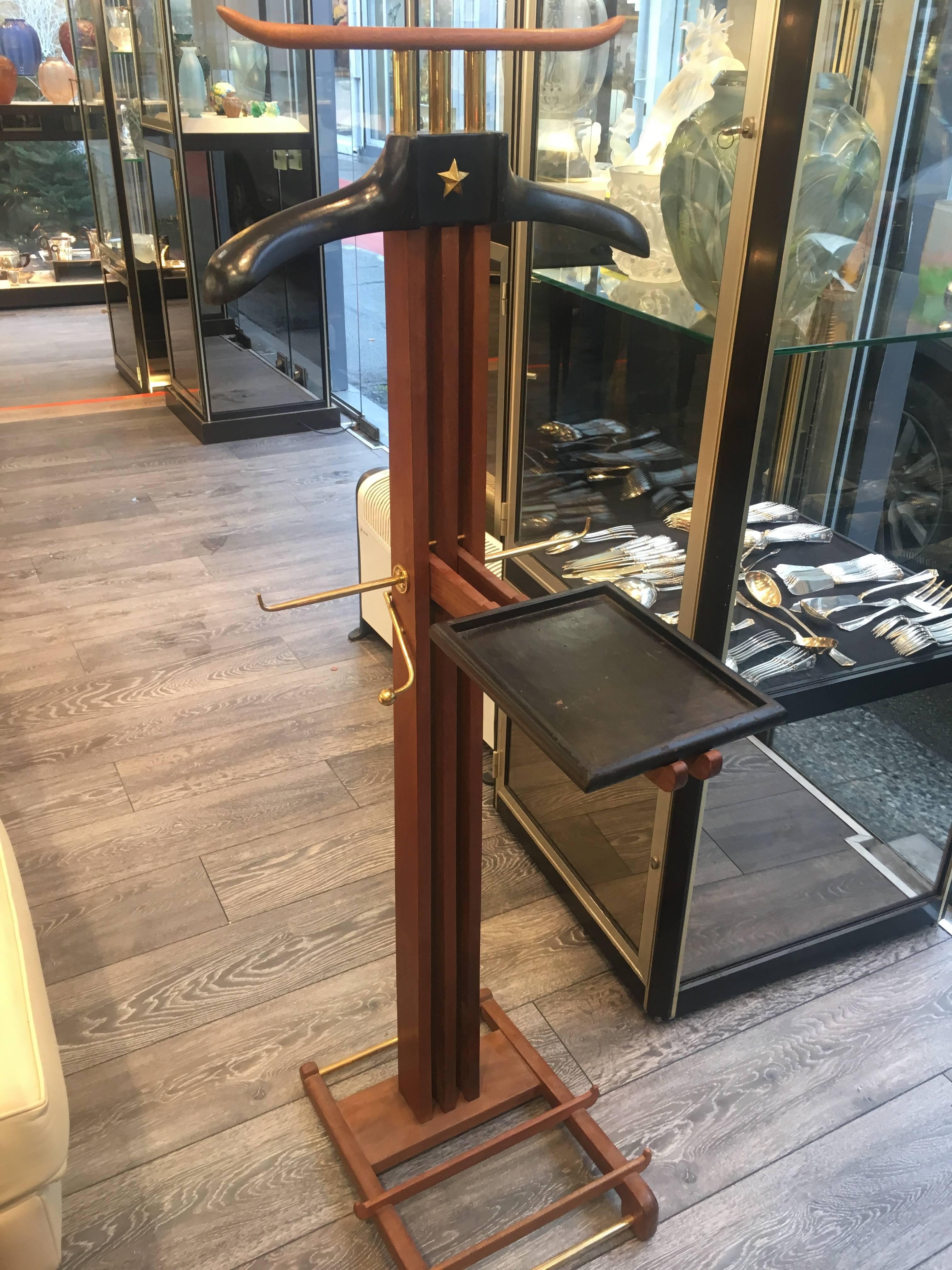 Night valet made out of all-wood mahogany. The shaft with its three studs decorated with an open work design receives within its centerline a small foldaway table covered in black leather. The clothe hanger made out of black leather is topped by