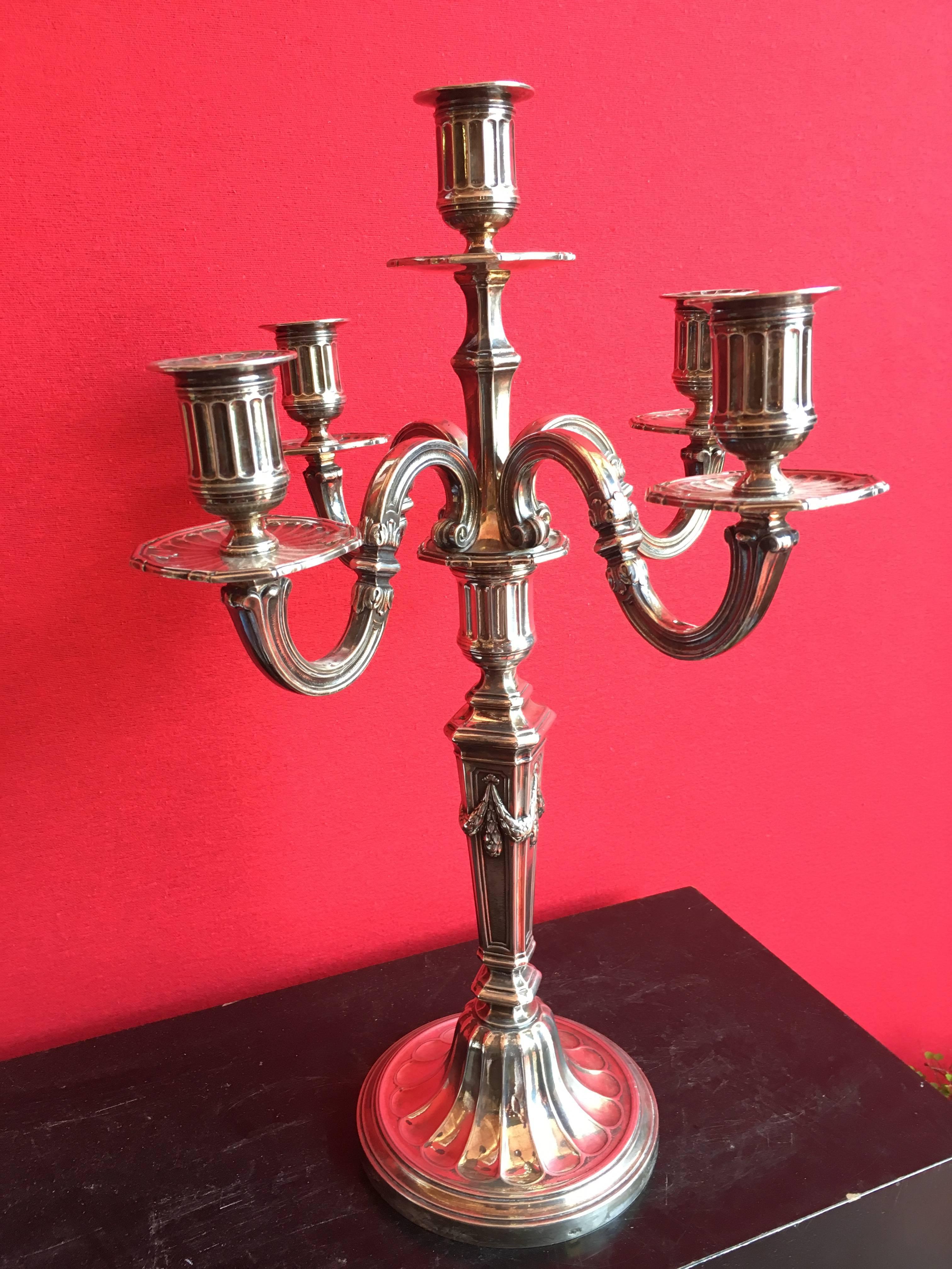 Pair of candlesticks in silvered bronze with five arms of light, the pediment with grooves in recall on the binets, the barrel with flaps decorated with laurels in falls. The base beaded decor and a frieze of laurels is topped with fût from which