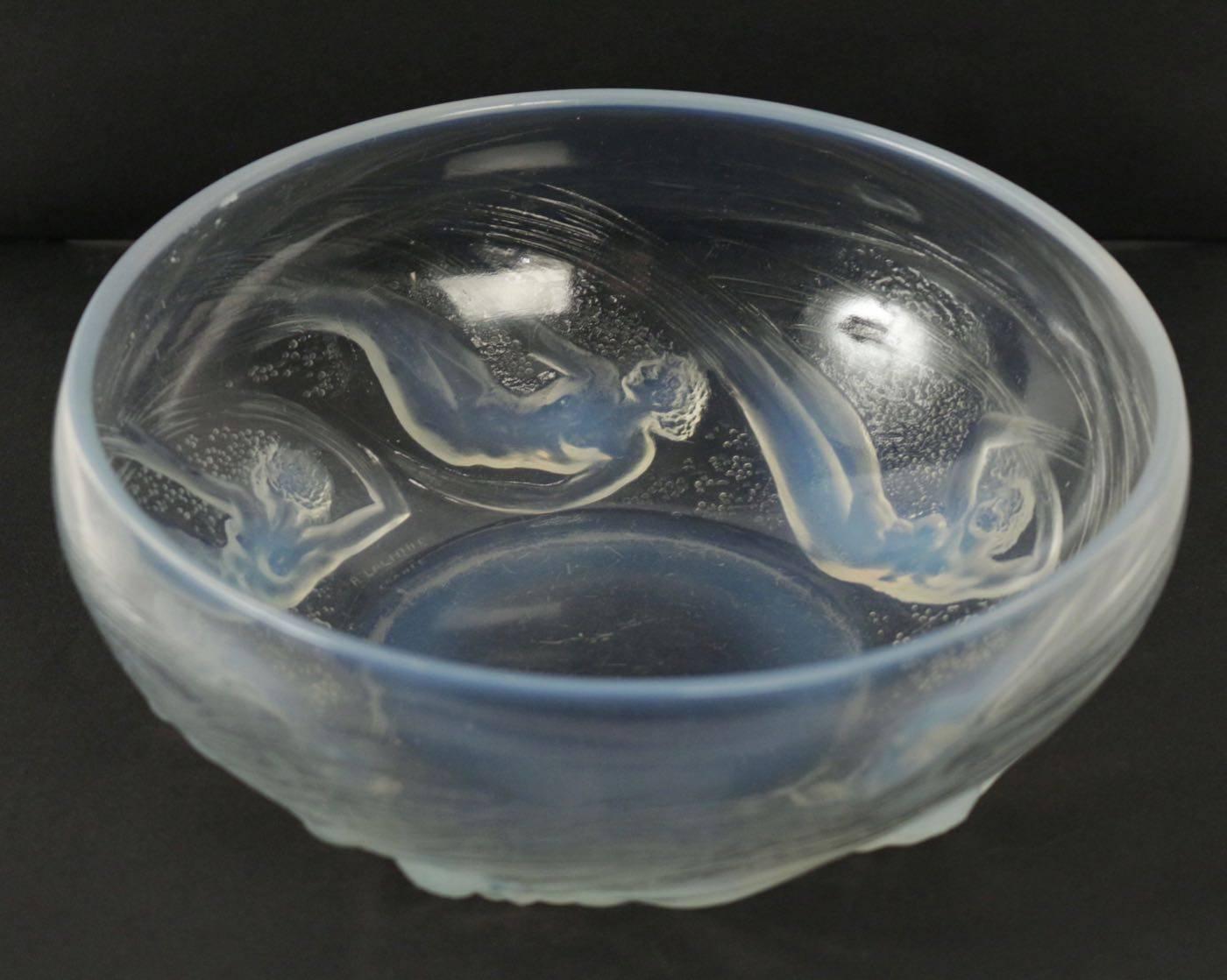 Wide opalescent and frosted round glass with a design of six mythical nude female type figures (Ondines) in various swirling possess around the bowl
Model created in 1921
signed R Lalique engraved
Bibliographie: F. Marcilhac, , réf. N°380, p. 292.