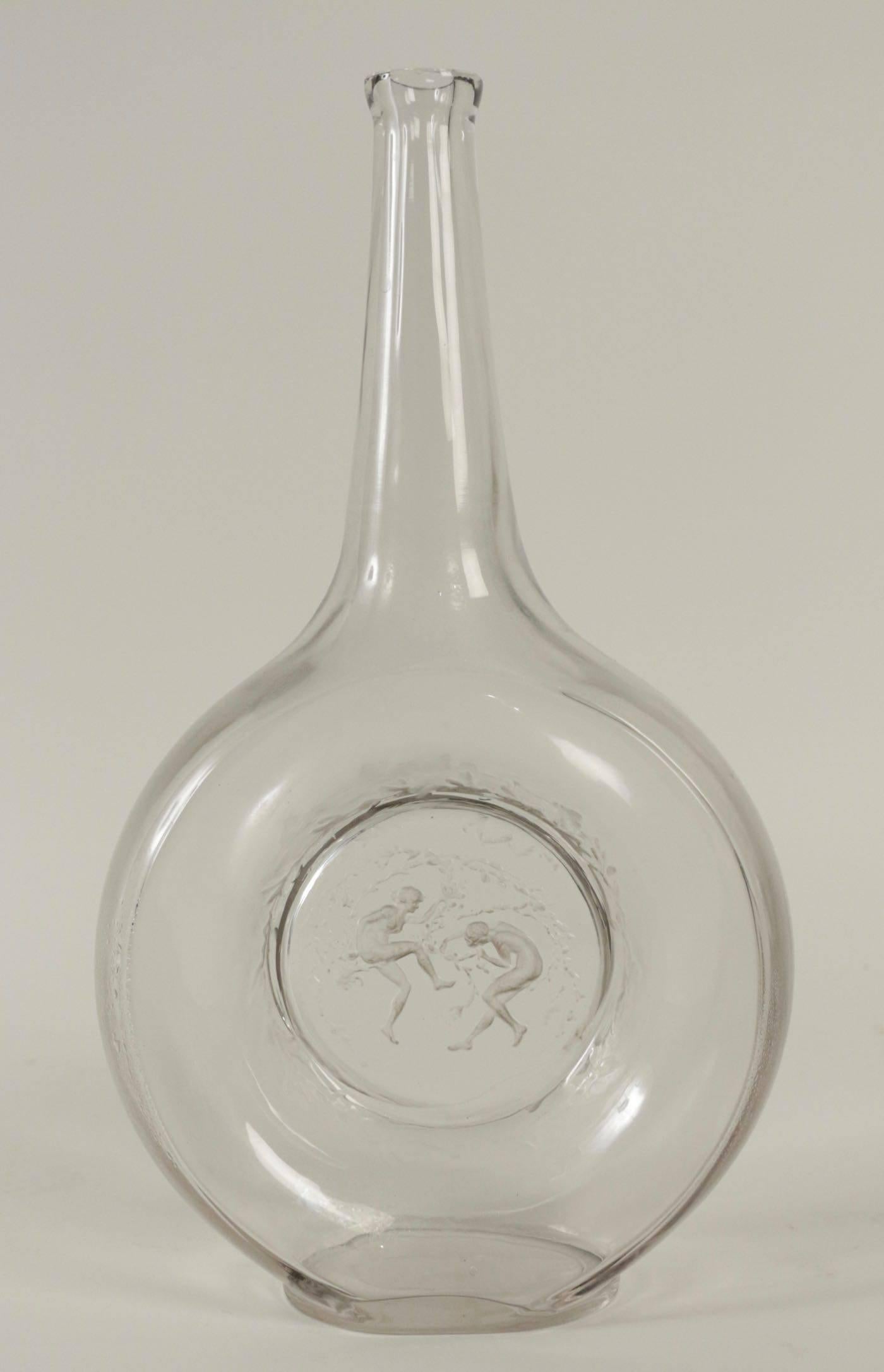 Clear glass long necked R. Laique decanter with the circular lower section having a central design of two dancers
hand writing signature
Lalique Carafe Deux Danseuses: 13 and 1/4 inches tall clear glass with a recessed central design of two