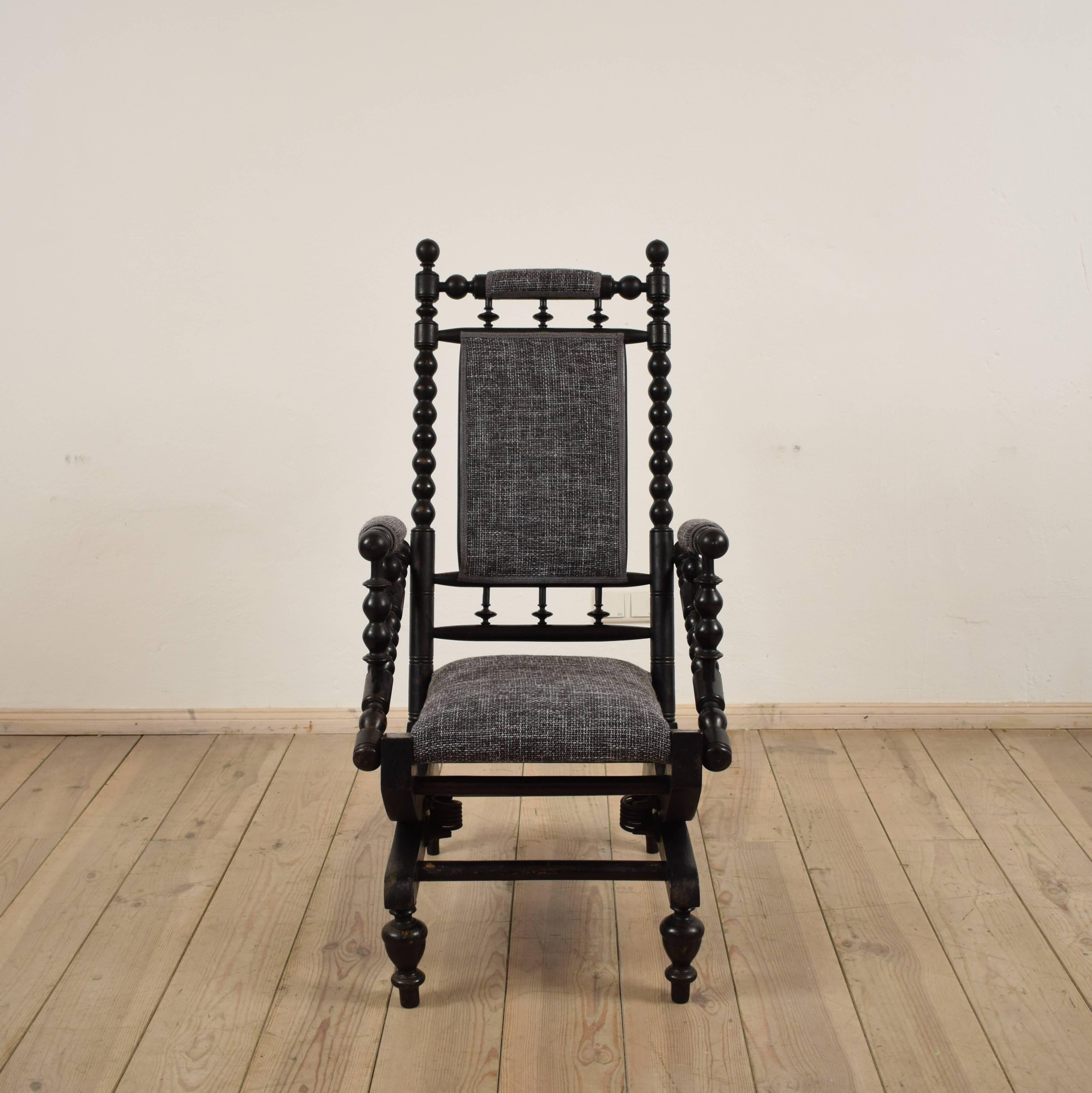 A late 19th century Victorian mahogany American rocking chair. The chair is in ash which is black lacquered. As well the armchair has bobbin spindles to the arms and frame and it is re-upholstered with a thick black fabric. The chair is sitting on