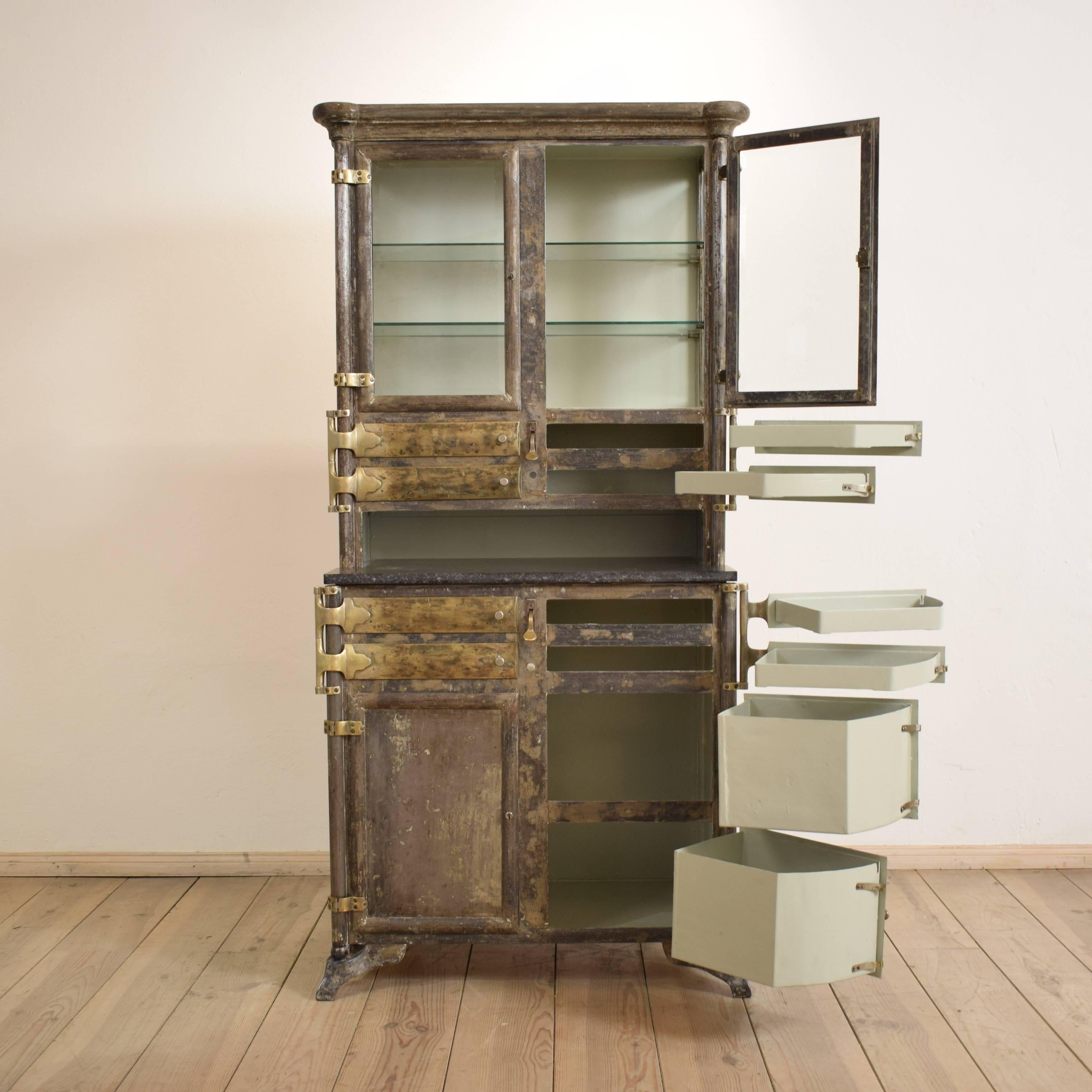 This dental cabinet from the 1920s is made out of metal and has brass swingable drawers. It has got the original glass with a facet cut.
It was made by the German manufacturer 