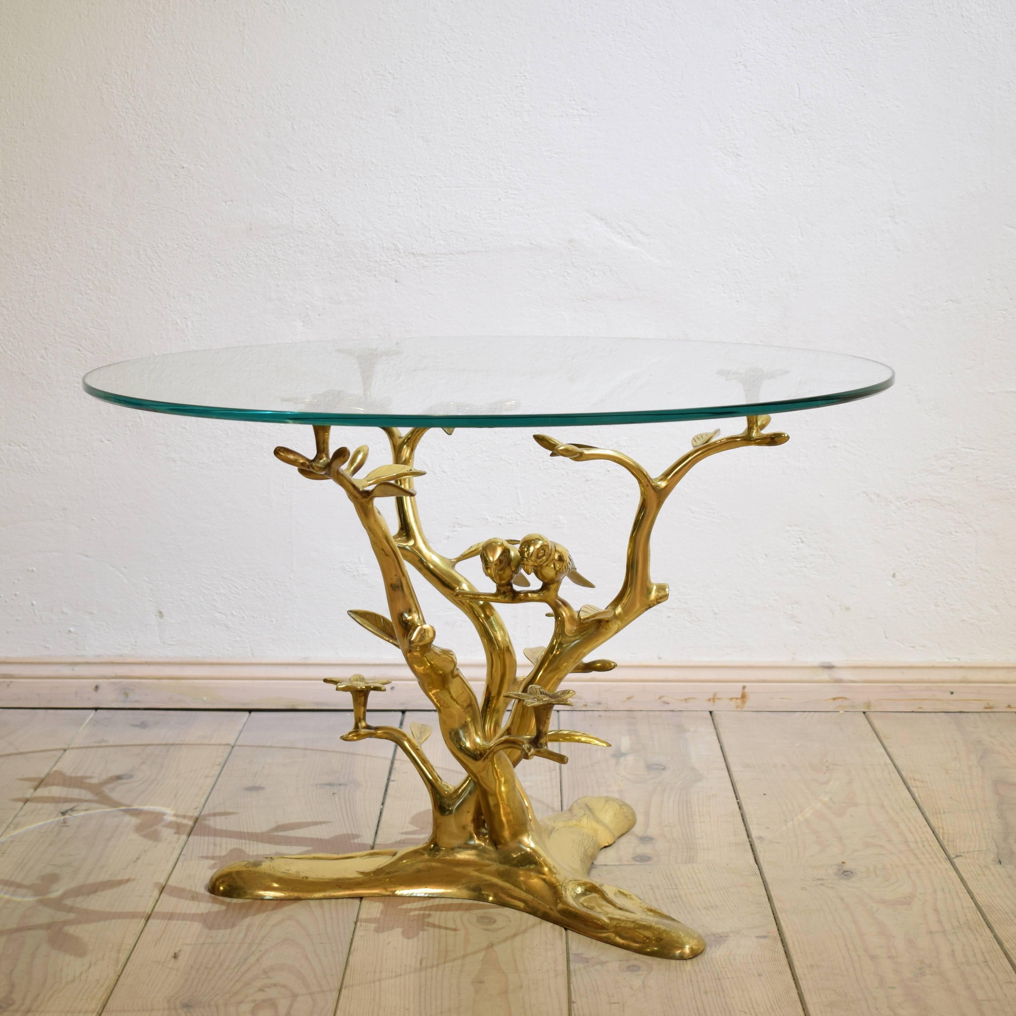 This coffee table by Willy Daro with the organic tree form with flowers and pair birds. Table base has a circular glass top. The table features a sculptural brass base with branches and leaves. The table is a great piece, and is pretty to look at