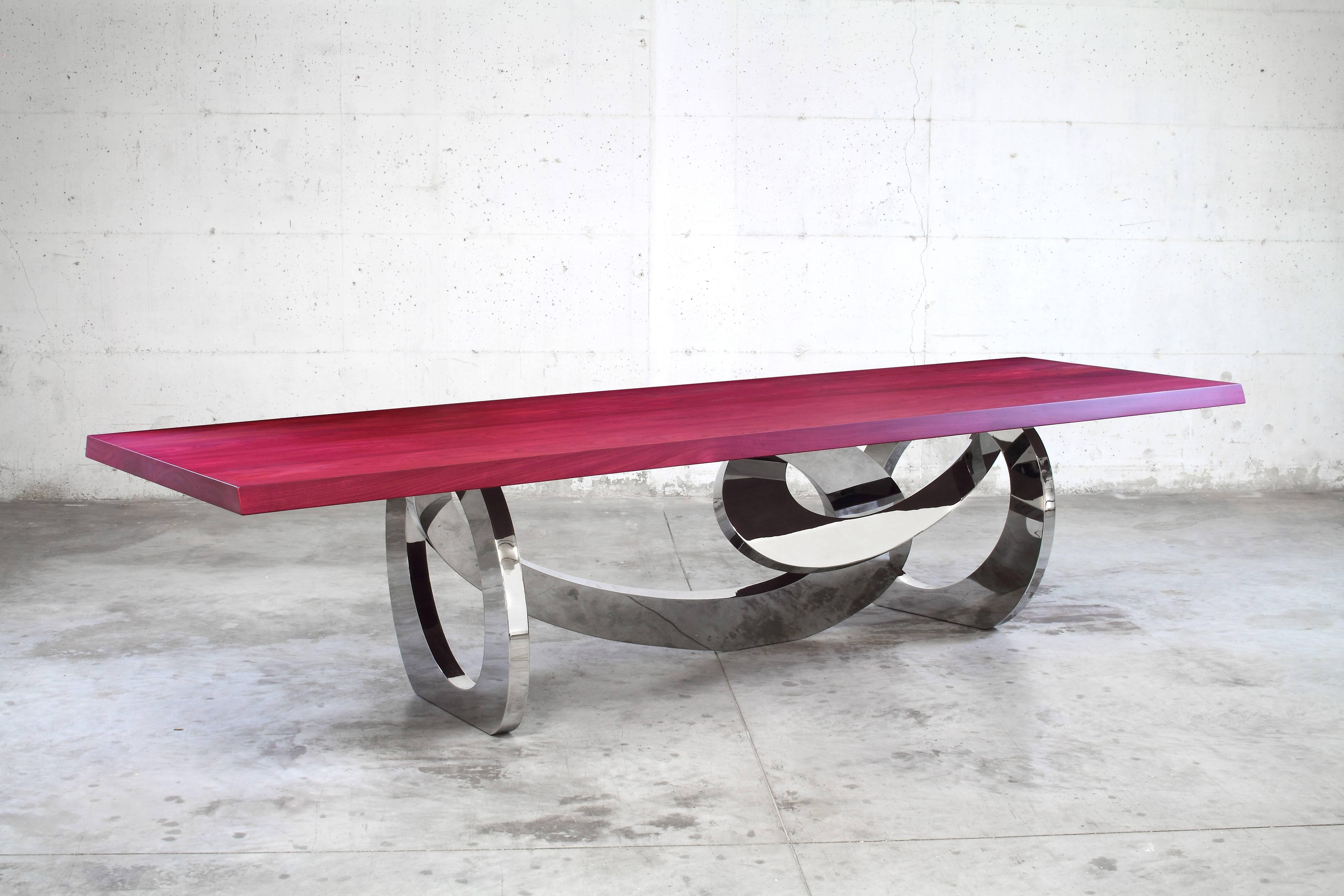 Il tavolo 'Woodele' è un importante tavolo da pranzo con struttura in acciaio inox lucidato a specchio e piano in legno massello di Amaranto ( Purpleheart solid wood ). Ogni singolo braccialetto è saldato e lucidato a mano. La finitura a specchio