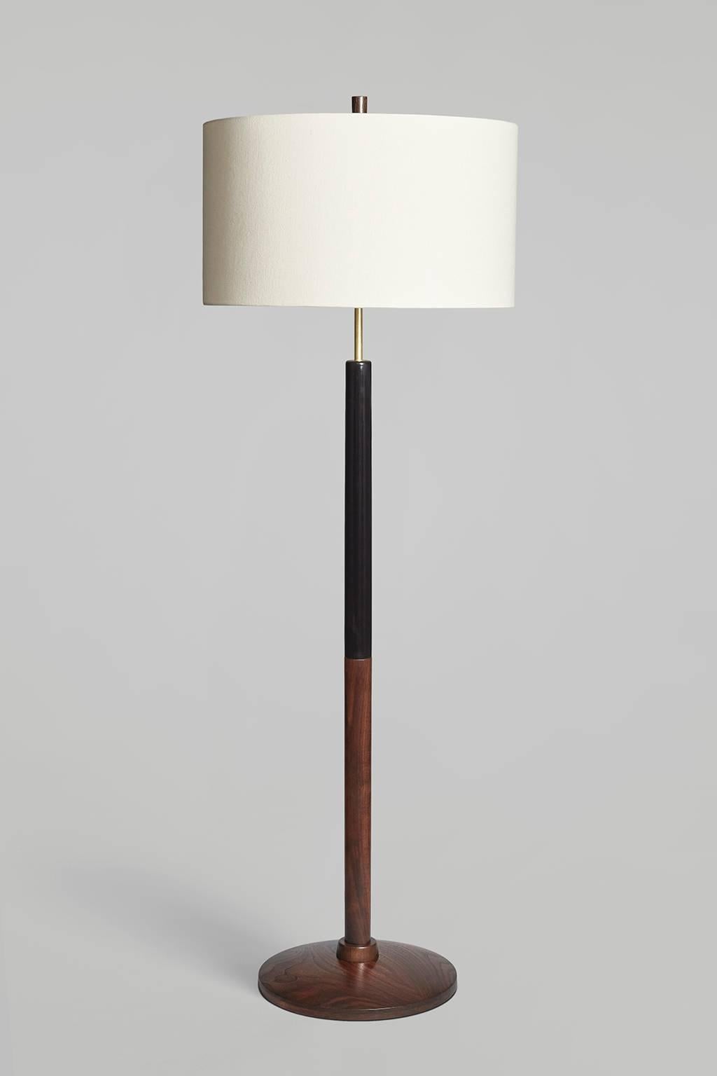 The Altmar I floor lamp pairs a warm, curving disc of figured walnut, with a spare, vertical form to hold its large shade. Base of walnut and ebonized maple, with a walnut neck and finial. Brass hardware, black fabric-covered cord, trimless, and