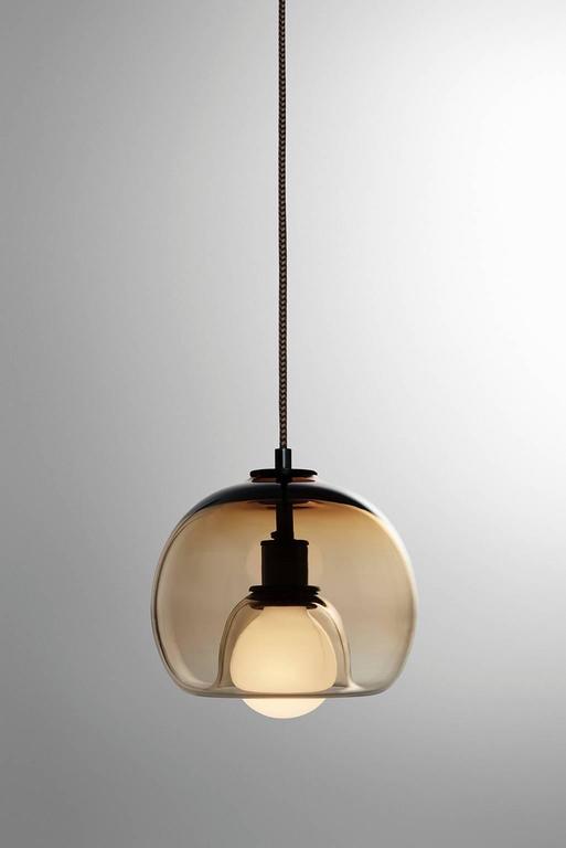 A handblown orb gracefully inverted to house a globe bulb, like a pearl encased in a glass oyster. The Eres bronze has an 8” diameter with a 4' black and brown houndstooth fabric-covered cord and a 4.75” diameter black porcelain canopy. Houses one
