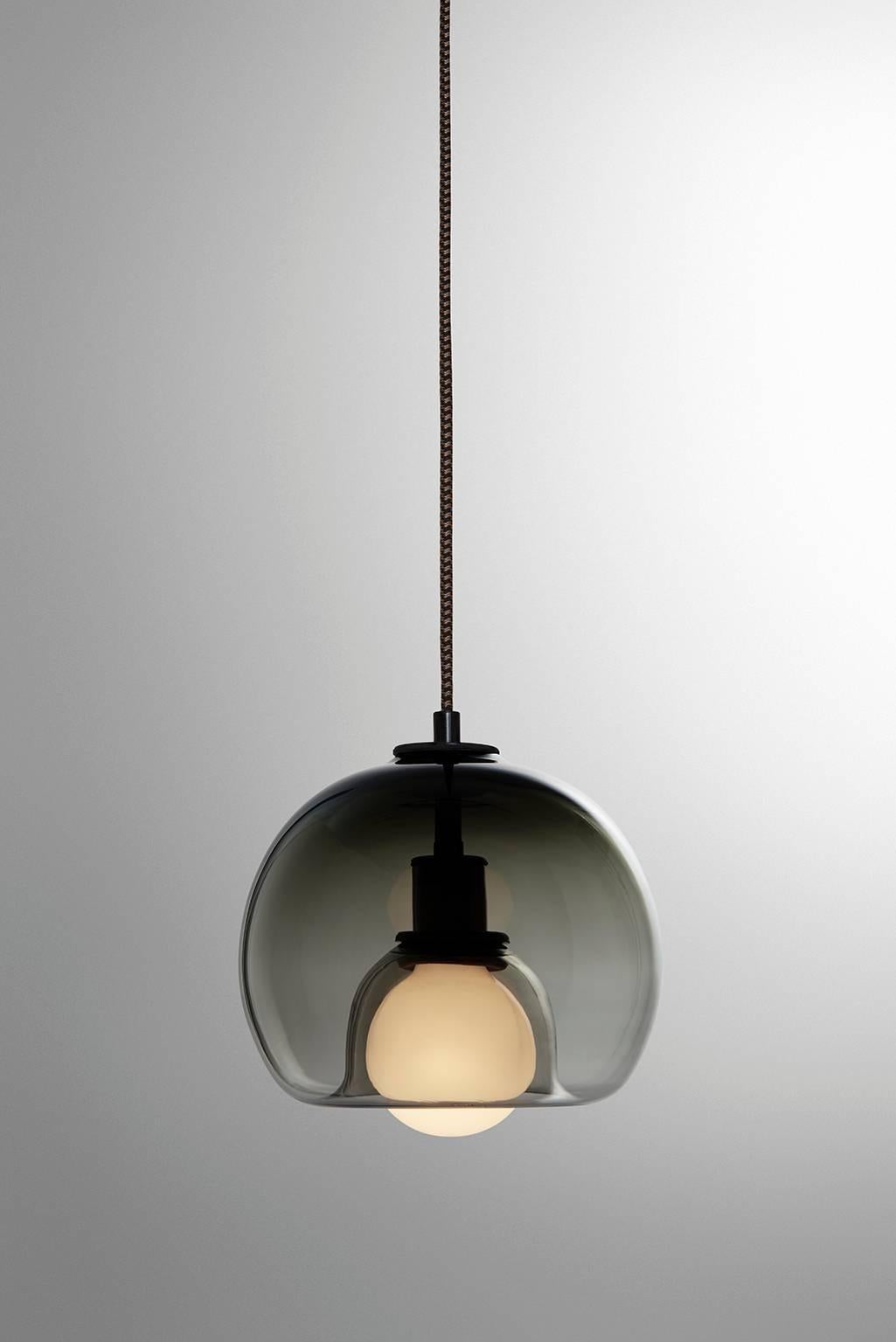 A handblown orb gracefully inverted to house a globe bulb, like a pearl encased in a glass oyster. The Eres Smoke has an 8” diameter with a 4' black and brown houndstooth fabric-covered cord and a 4.75” diameter black porcelain canopy. Houses one