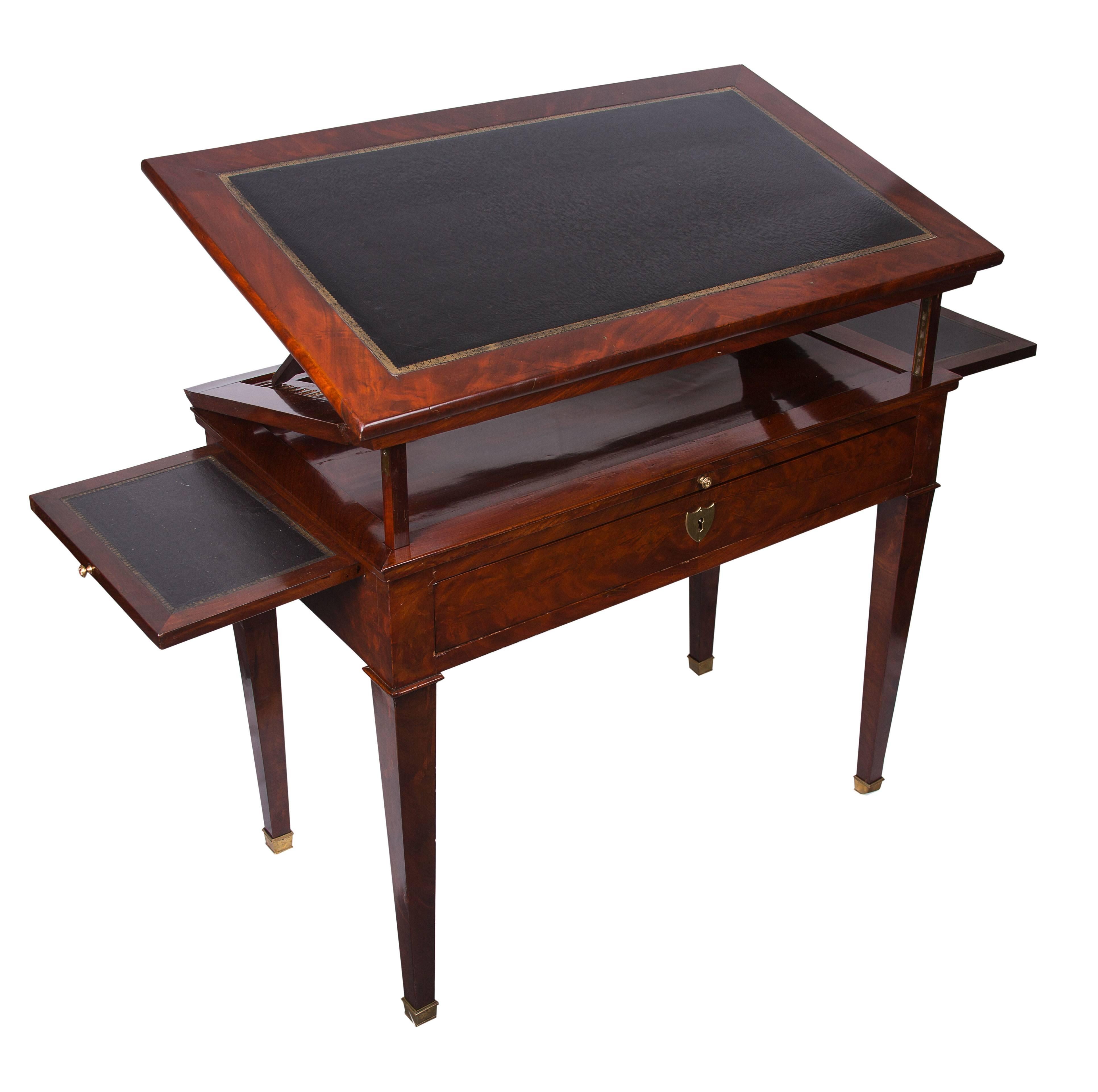 This is a superb early 19th century French Empire architect's desk and table having both a beautifully figured mahogany and tooled leather work surface. The table has a folding and ratcheted top above a frieze that is fitted with a central drawer