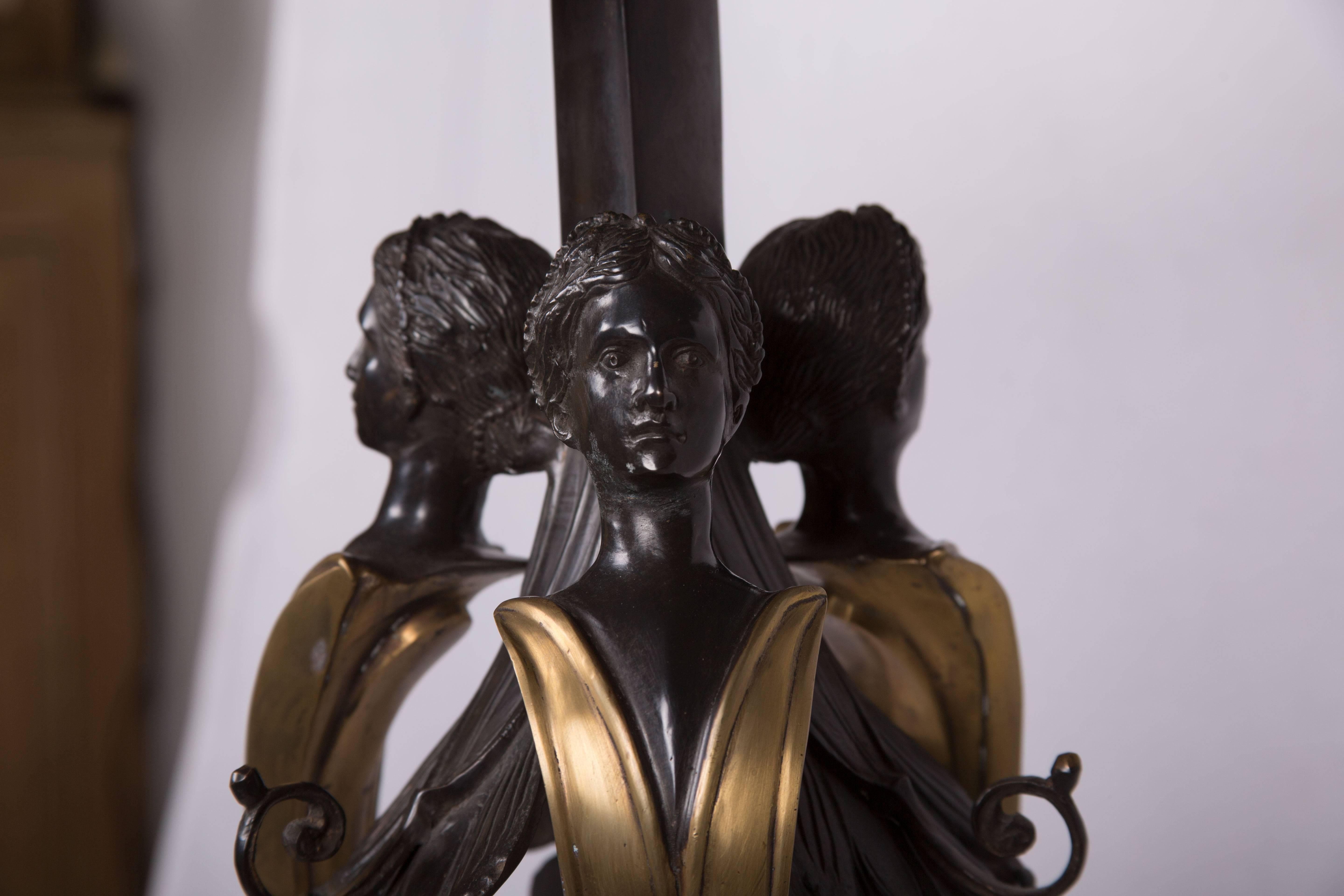 Pictured is a mid-20th century Empire style bronzed and burnished metal pedestal with a black marble top above three stylized caryatids centered over a long slender metal tripod with a triangular stretcher joining the feet.