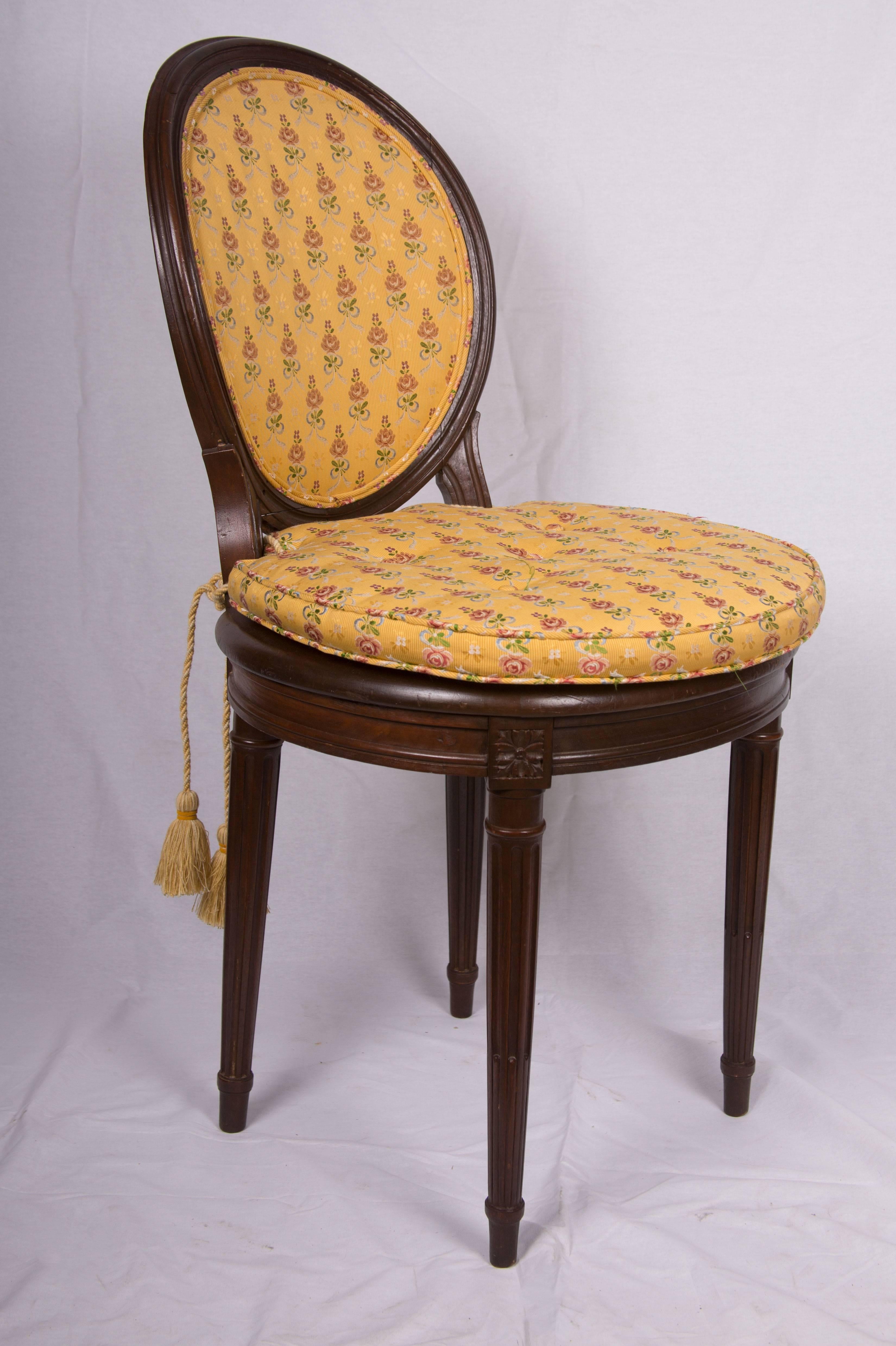 This is a pair of Louis XVI style walnut musician's chairs with upholstered open backs and caned seats with loose cushions upholstered in identical fabric above prominent frieze and raised on round tapering fluted legs, late 19th century.