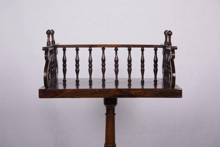 This is a picture of an English Regency book caddy with spindle divider joined by spindled ends and finials on top of end rails, supported by later mahogany round turned pedestal and out-scrolled feet, circa 1830.