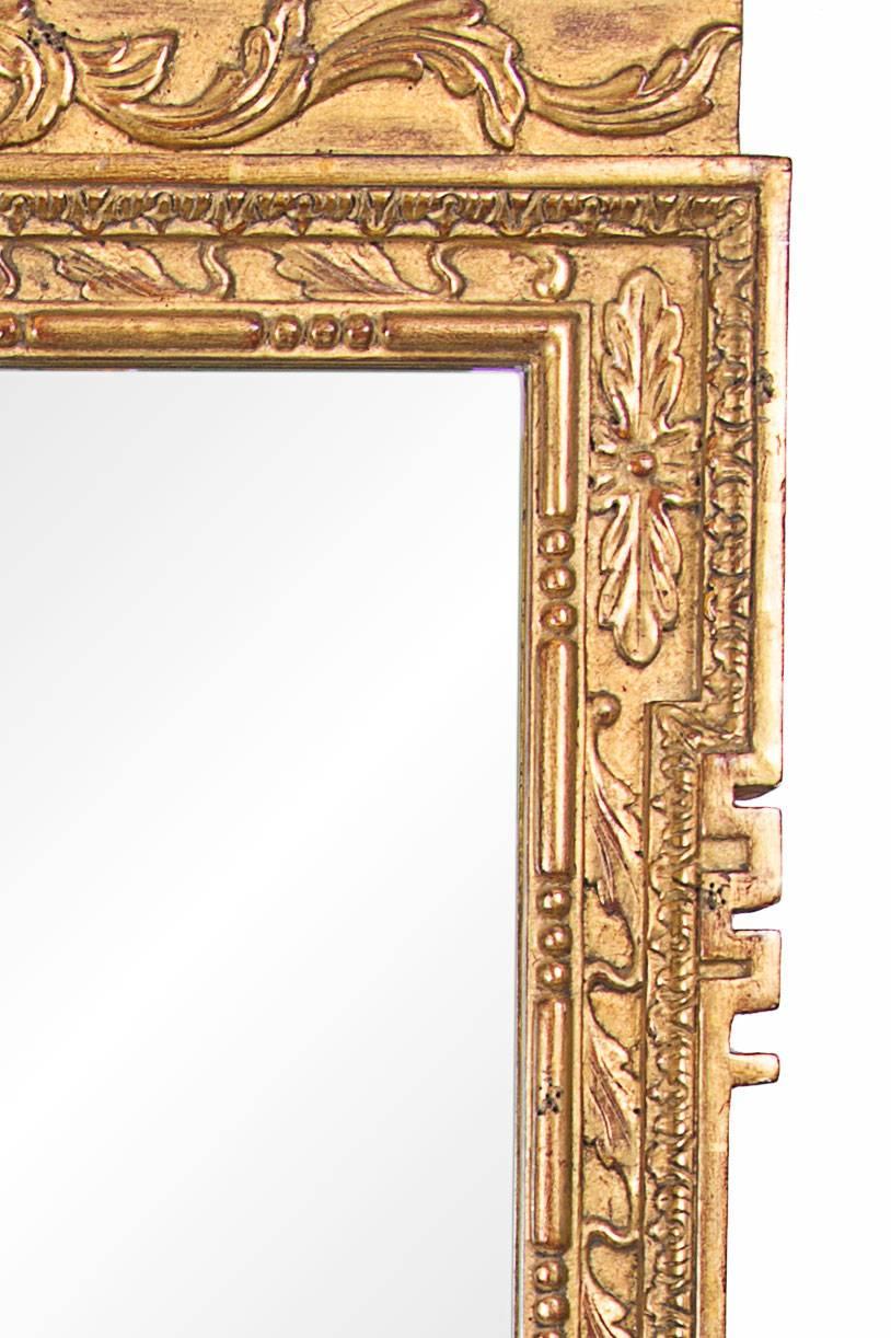 This magnificent English George II style hand-carved and gilt wall mirror has a rectangular mirror plate surrounded by a very fine architectural form of a broken arch pediment centered by a cluster of foliage in a shell form over a mirror plate