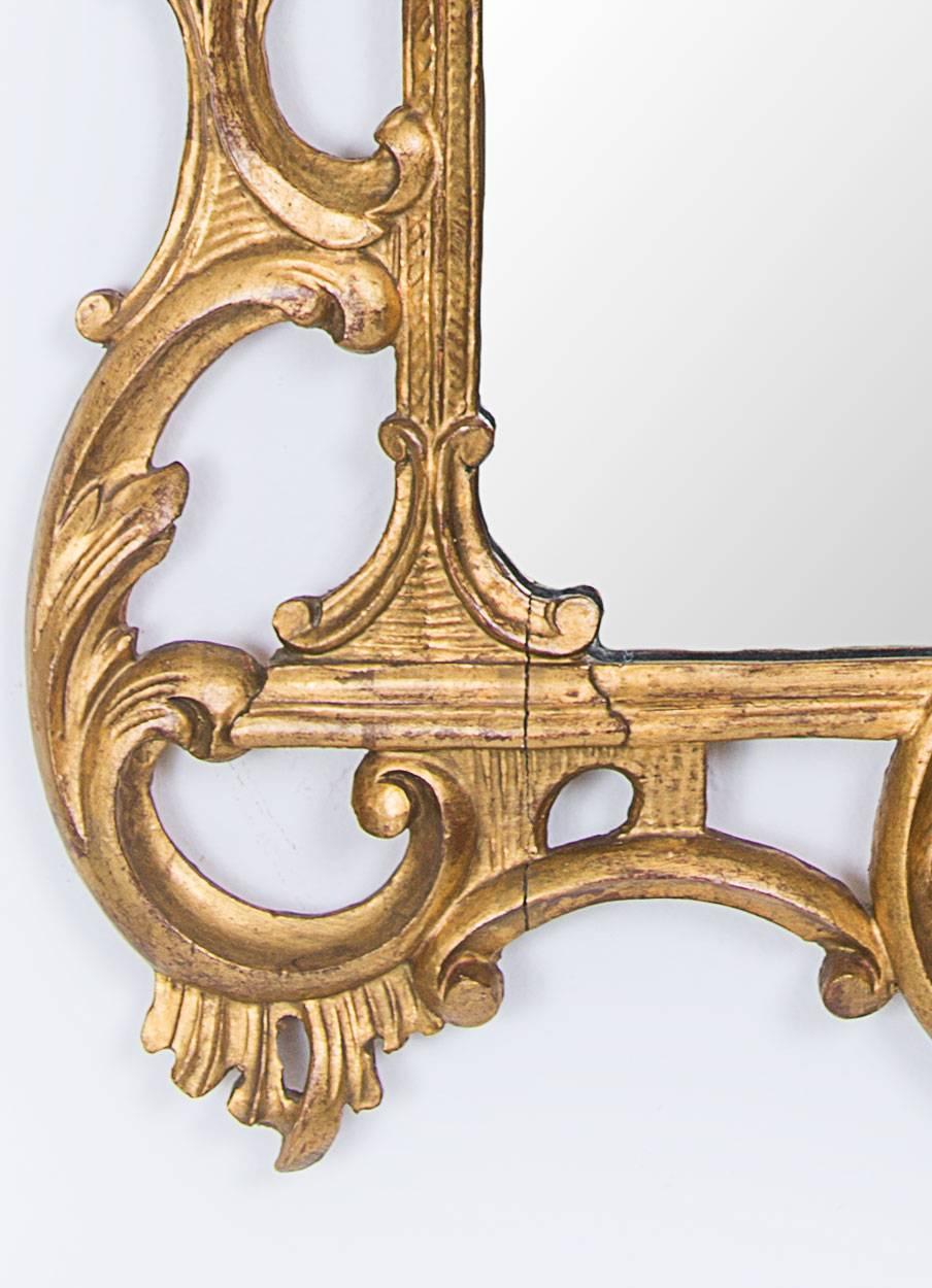 This George III style giltwood mirror has an open-work frame carved with flower heads and foliage centered by a prominent leaf motif cornice above a glass plate divided by a carved giltwood crossbar, early 20th century.