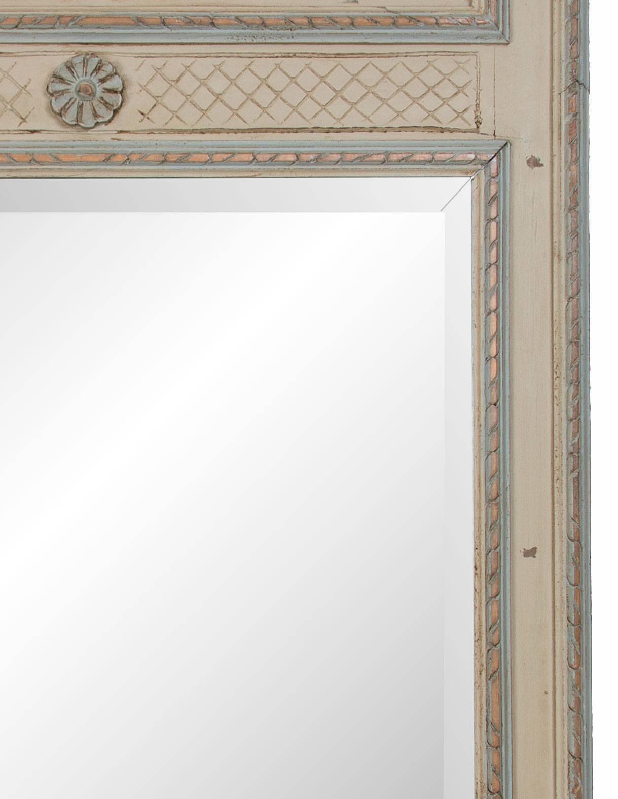 The neoclassical green painted trumeau shows an architectural decorated embossed panel at the top over a glass plate all within a wooden frame, late 20th century.