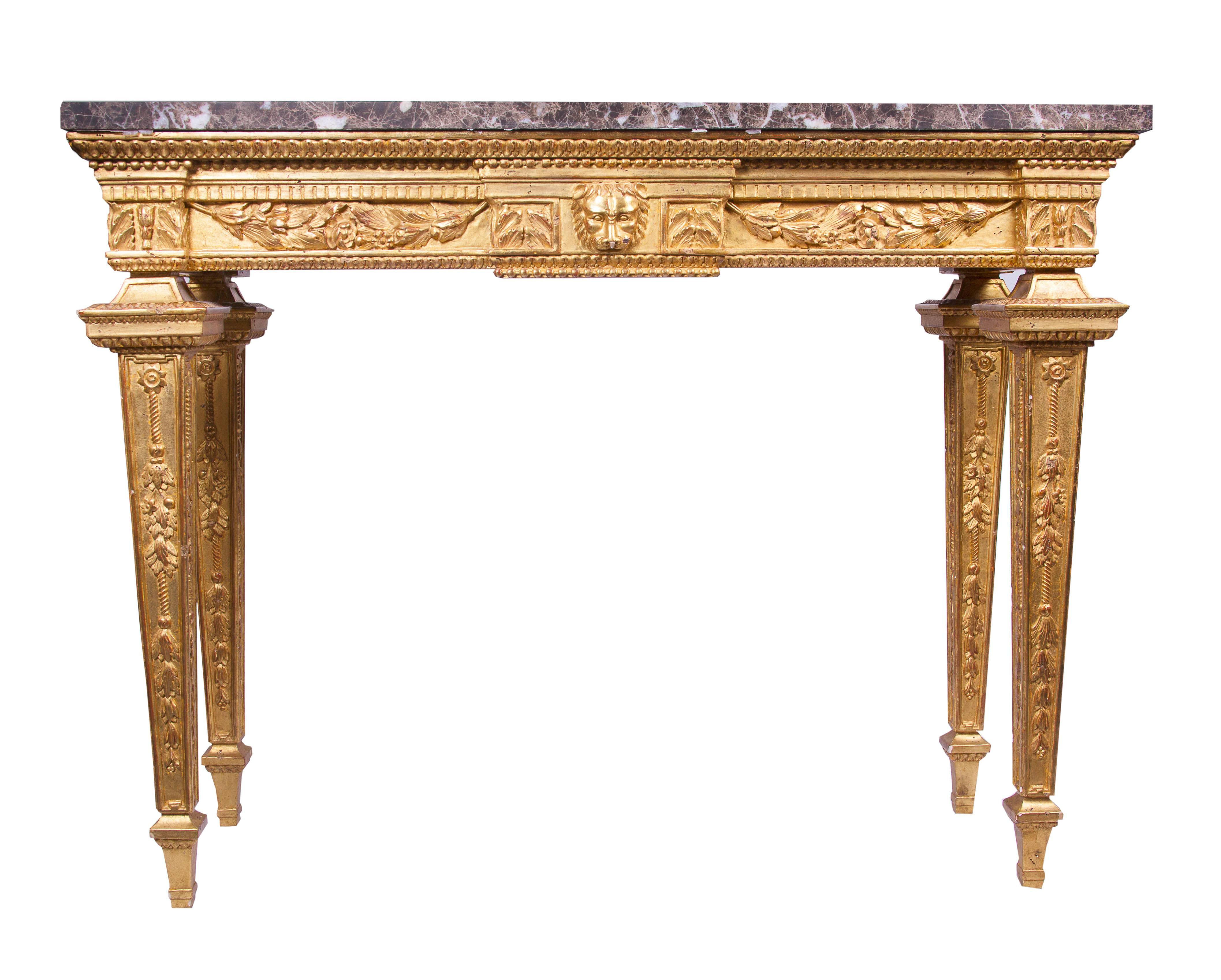 This stately pair of gilt consoles will make a statement of absolute sophistication. They are hand-carved in relief form followed by a gesso and fine gilt application. They are Louis XVI style showing a central lion mask flanked by swags. The top