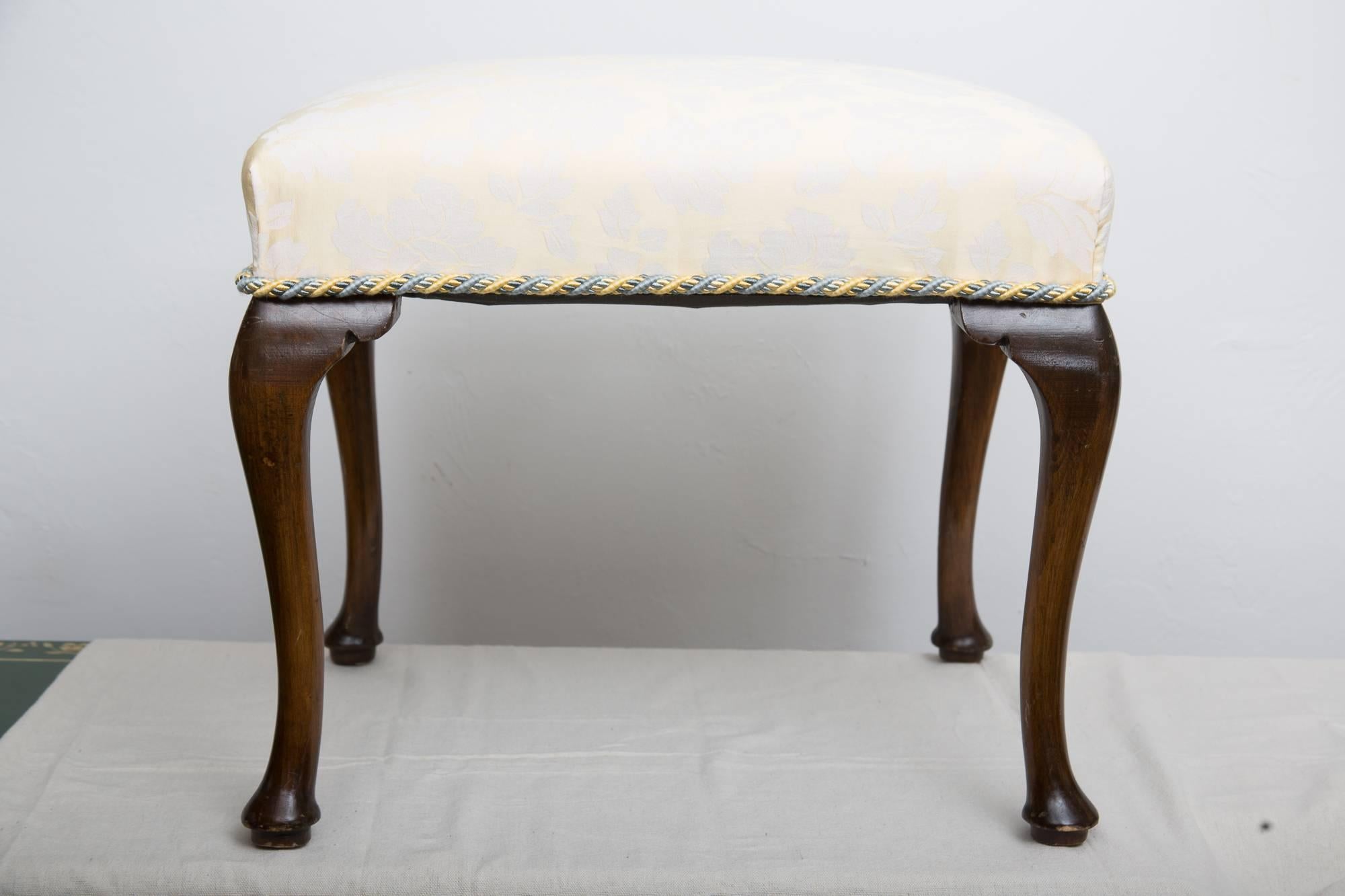 These lovely Queen Anne style benches have a light yellow damask-upholstered top accented with a braided trim intertwining blue and yellow supported by four walnut cabriole legs, early 20th century.