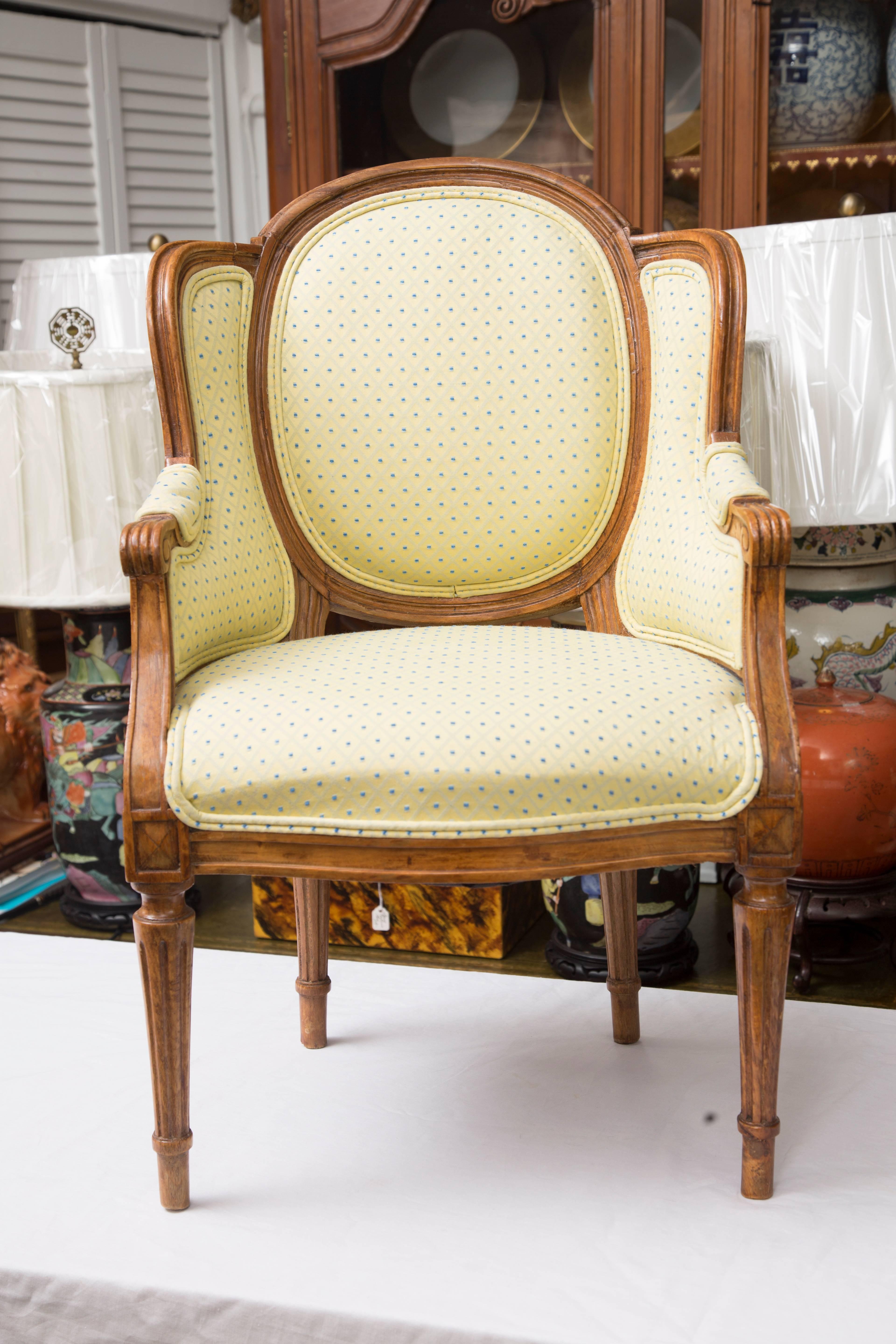 This is a charming pair of diminutive Louis XVI beechwood wing chairs with upholstered sides, back and seat, raised on round fluted legs, circa 20th century.