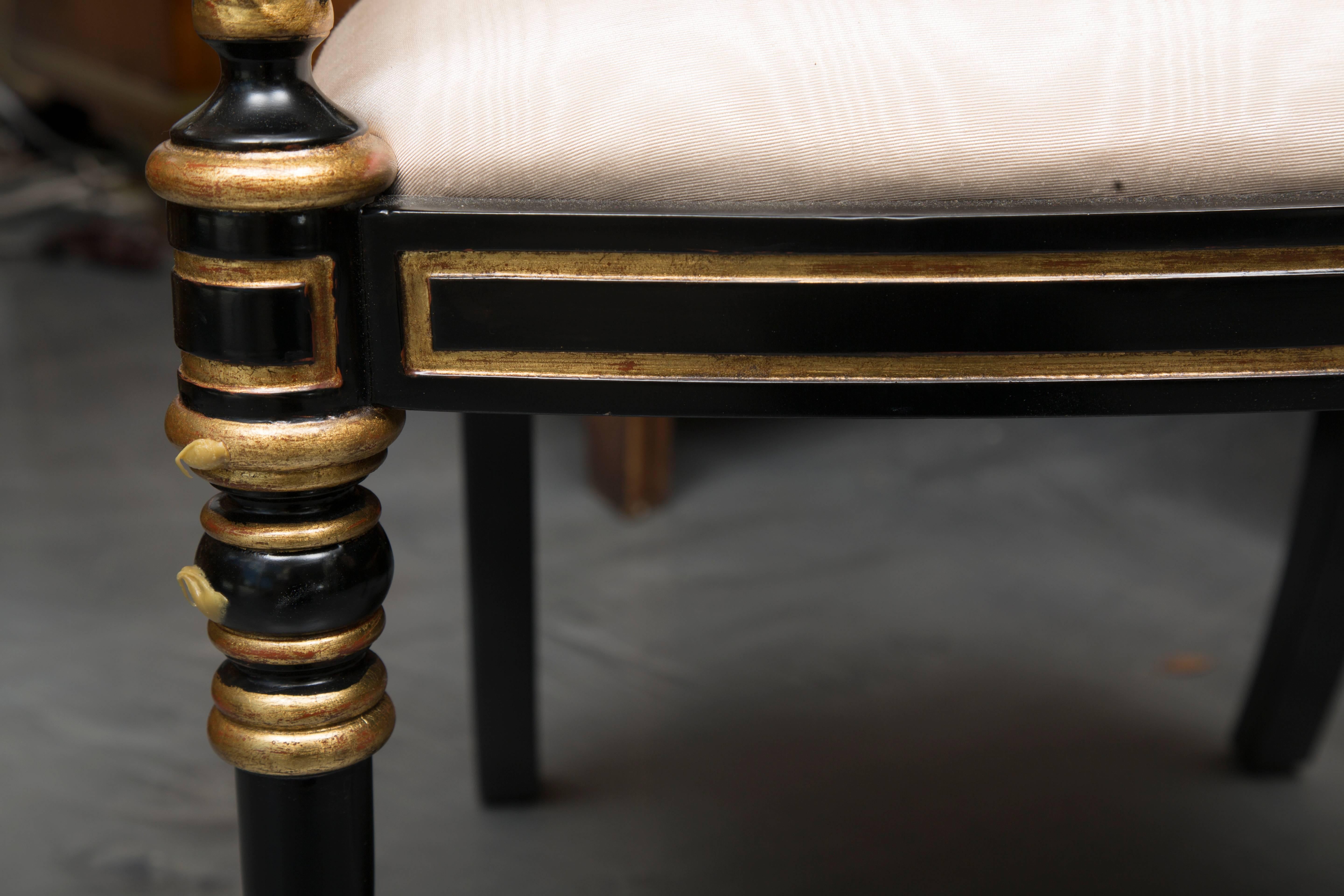This stately pair of Regency style ebonized and parcel-gilt armchairs has a simple top rail above a back-splat flanked by out-scrolling arms above a padded seat and supported by round tapering legs, circa 20th century.