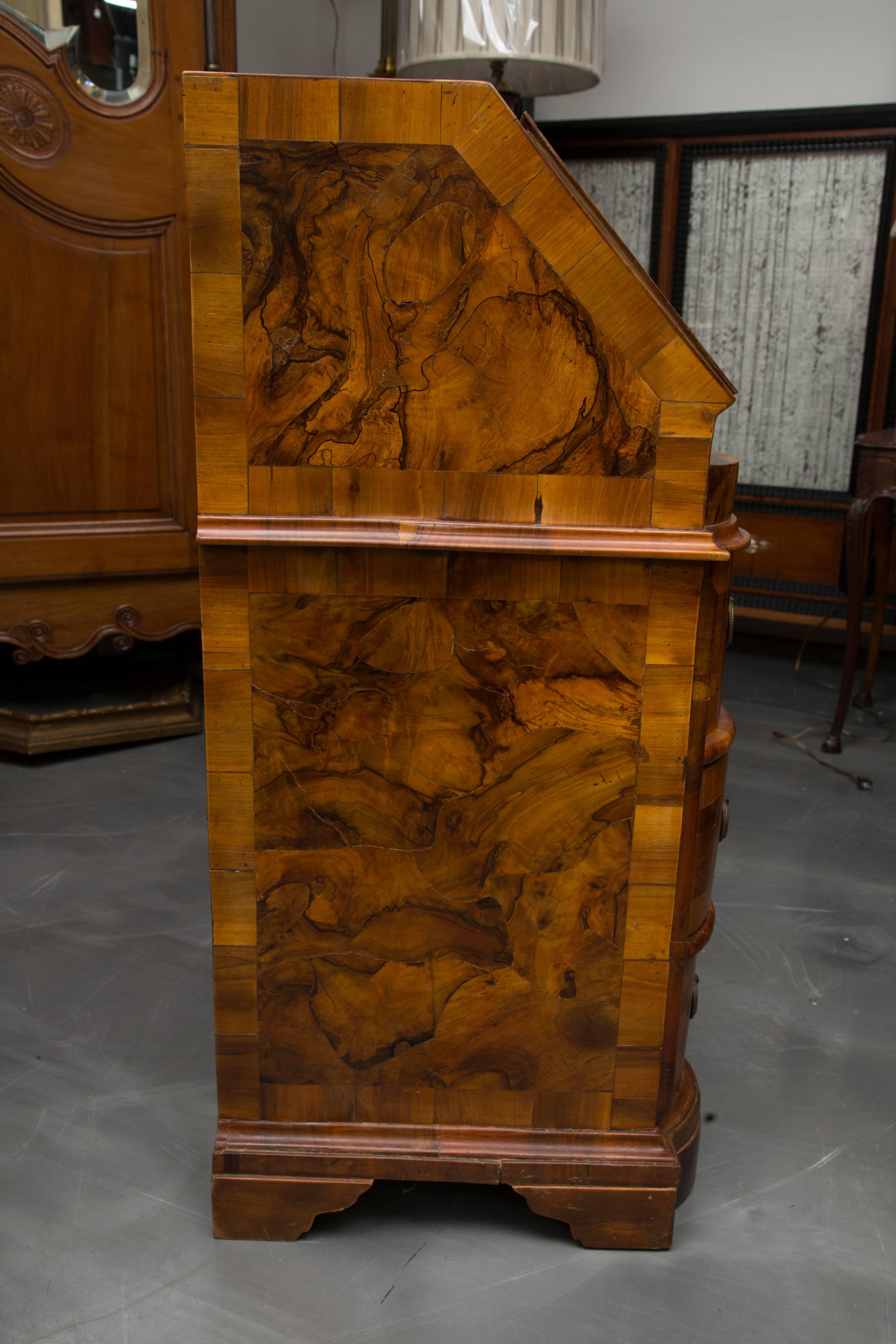 This exquisite Italian Rococo burl walnut desk has a slant front opening to reveal a central compartment with door flanked by small drawers above a serpentine frieze. Below are three conforming long graduated drawers separated by bold rounded