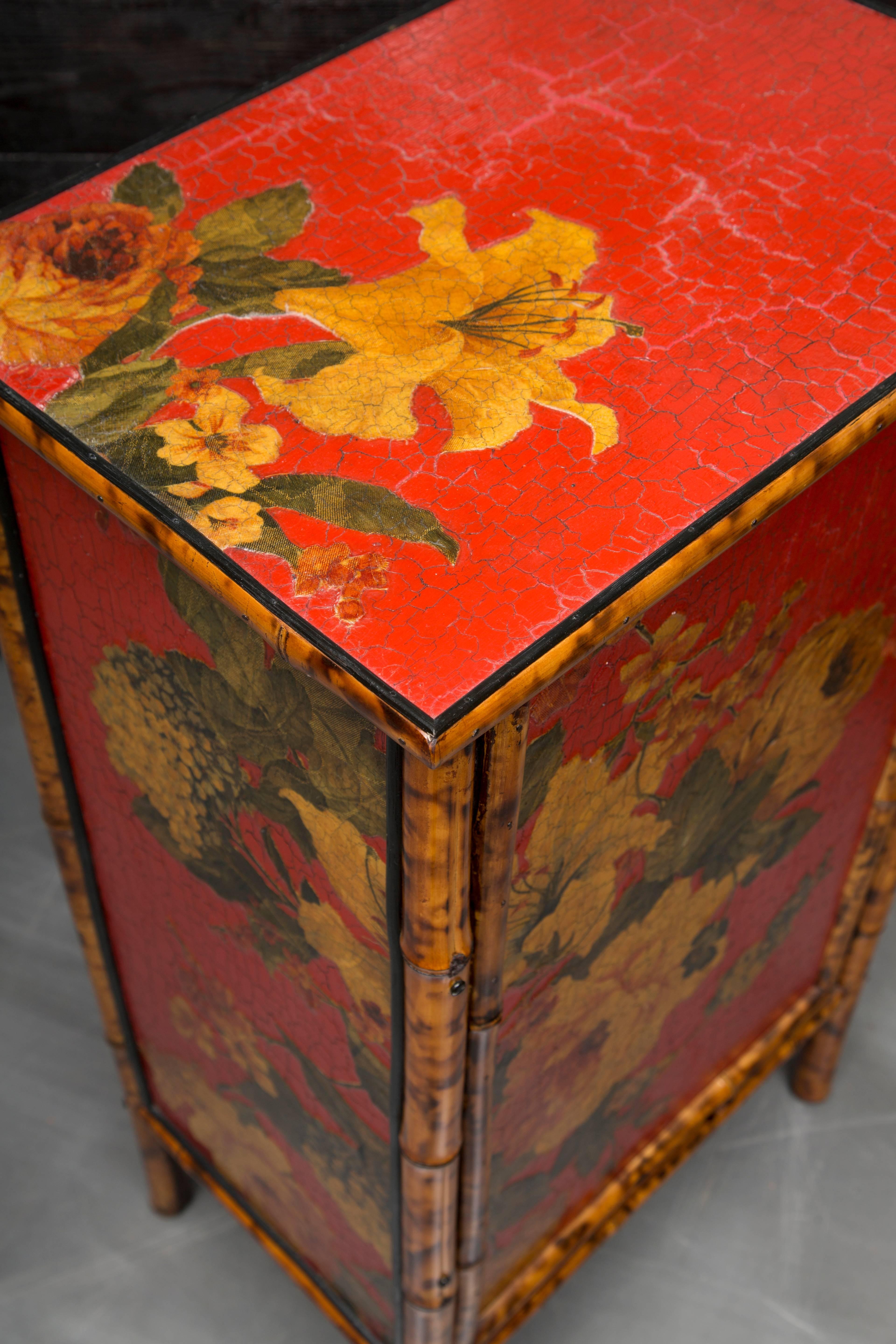 This decorative bamboo cabinet has a hand-painted yellow floral grouping on a red background with recurring images on the top and sides. The door opens to reveal interior shelving.